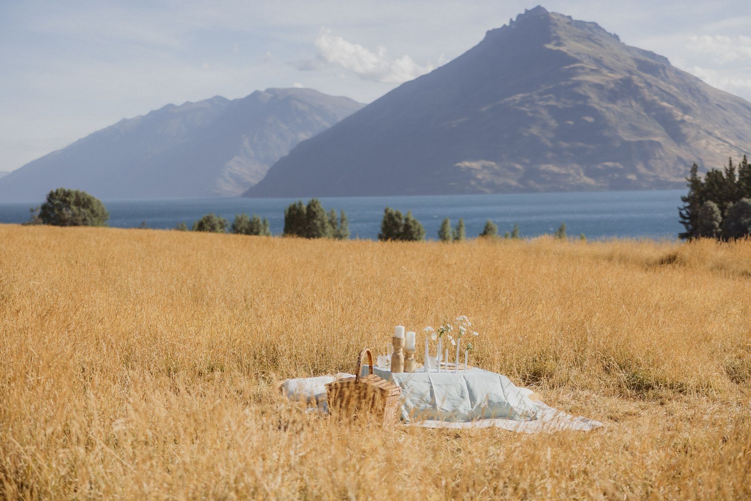 Scenic mountain landscape with golden fields and snow-capped peaks reflecting in a tranquil lake under blue skies.