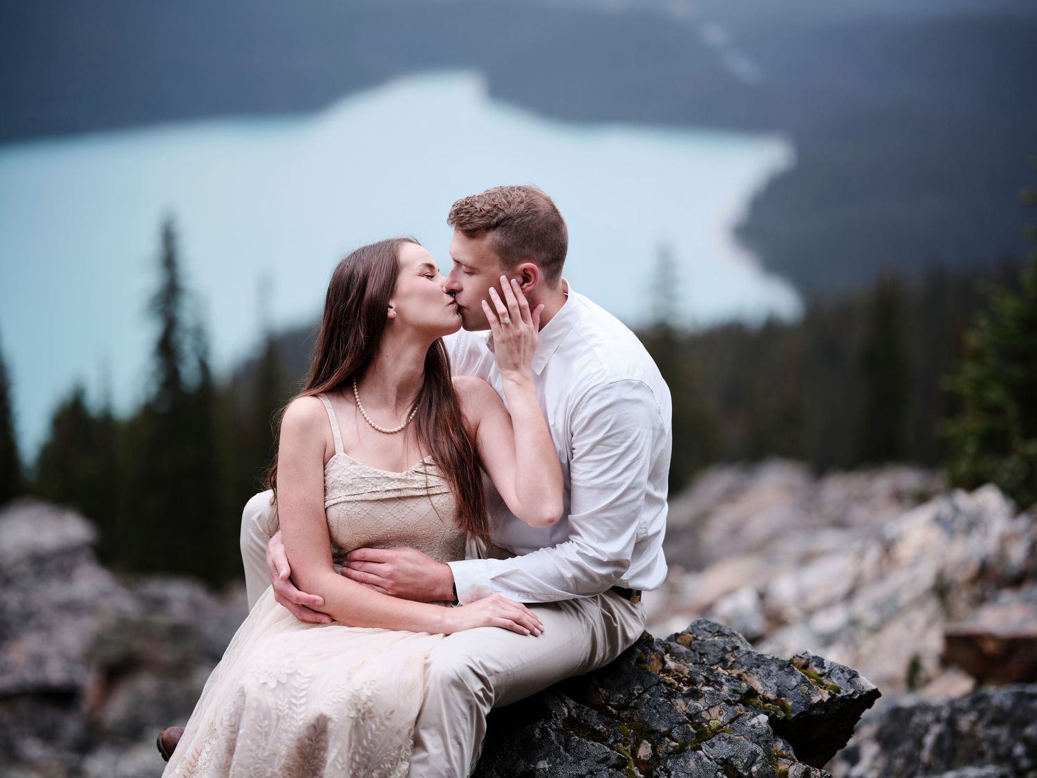 A romantic couple shares an intimate moment while sitting on rocks overlooking a misty mountain lake in Banff in the Canadian Rockies