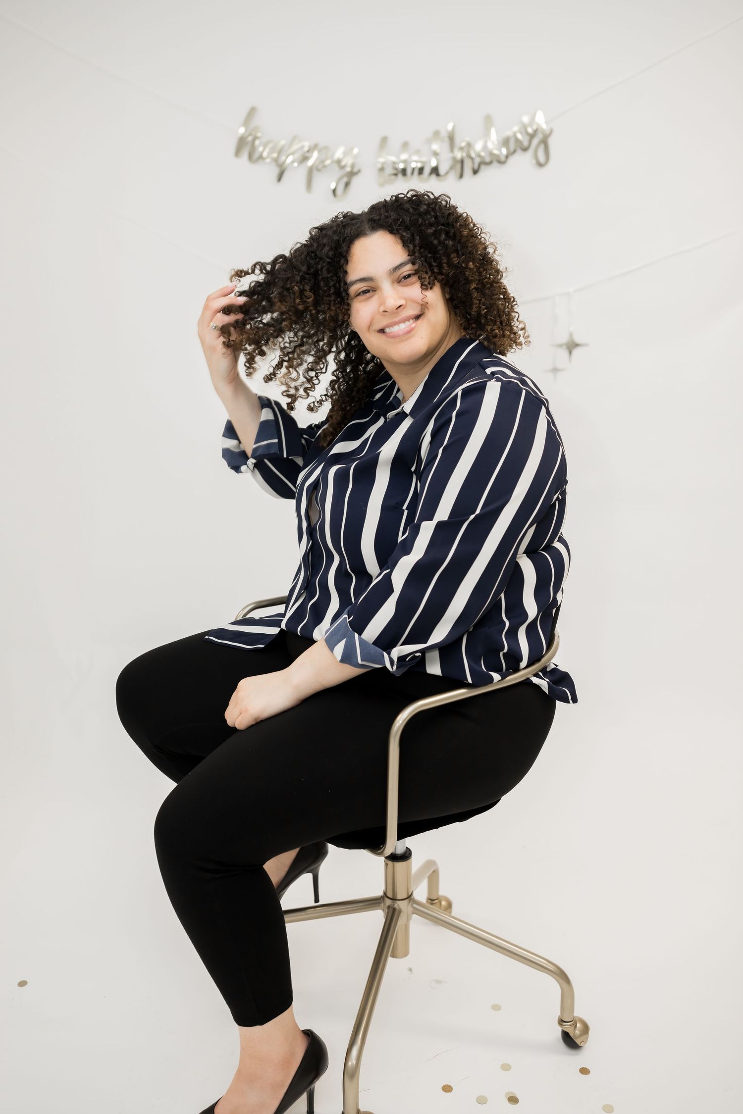 Casual studio portrait with striped navy blouse and black pants against white background.