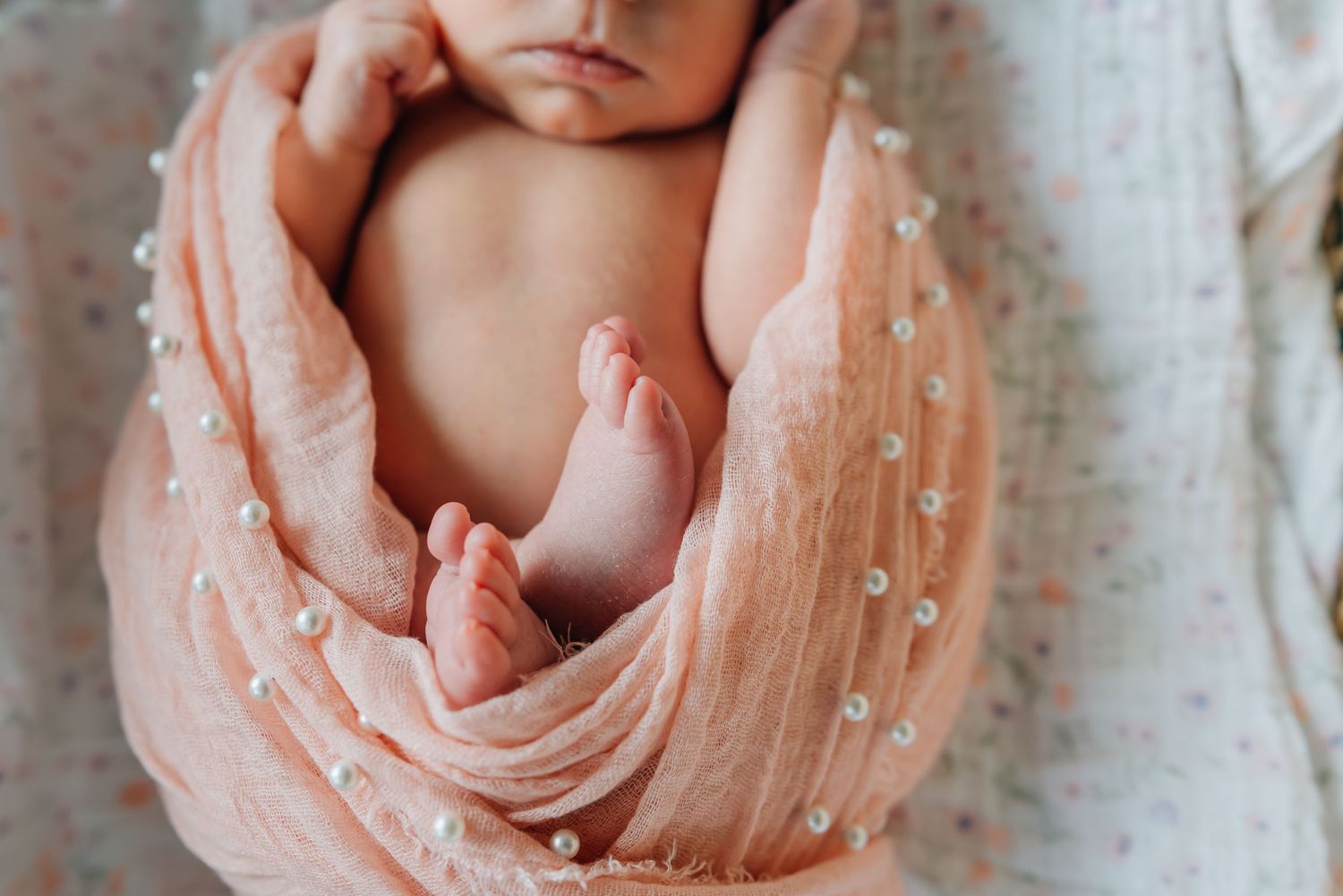 Lauren marie photography took a close up shot of a newborn baby girl's tiny feet as she's wrapped up in a pink wrap.