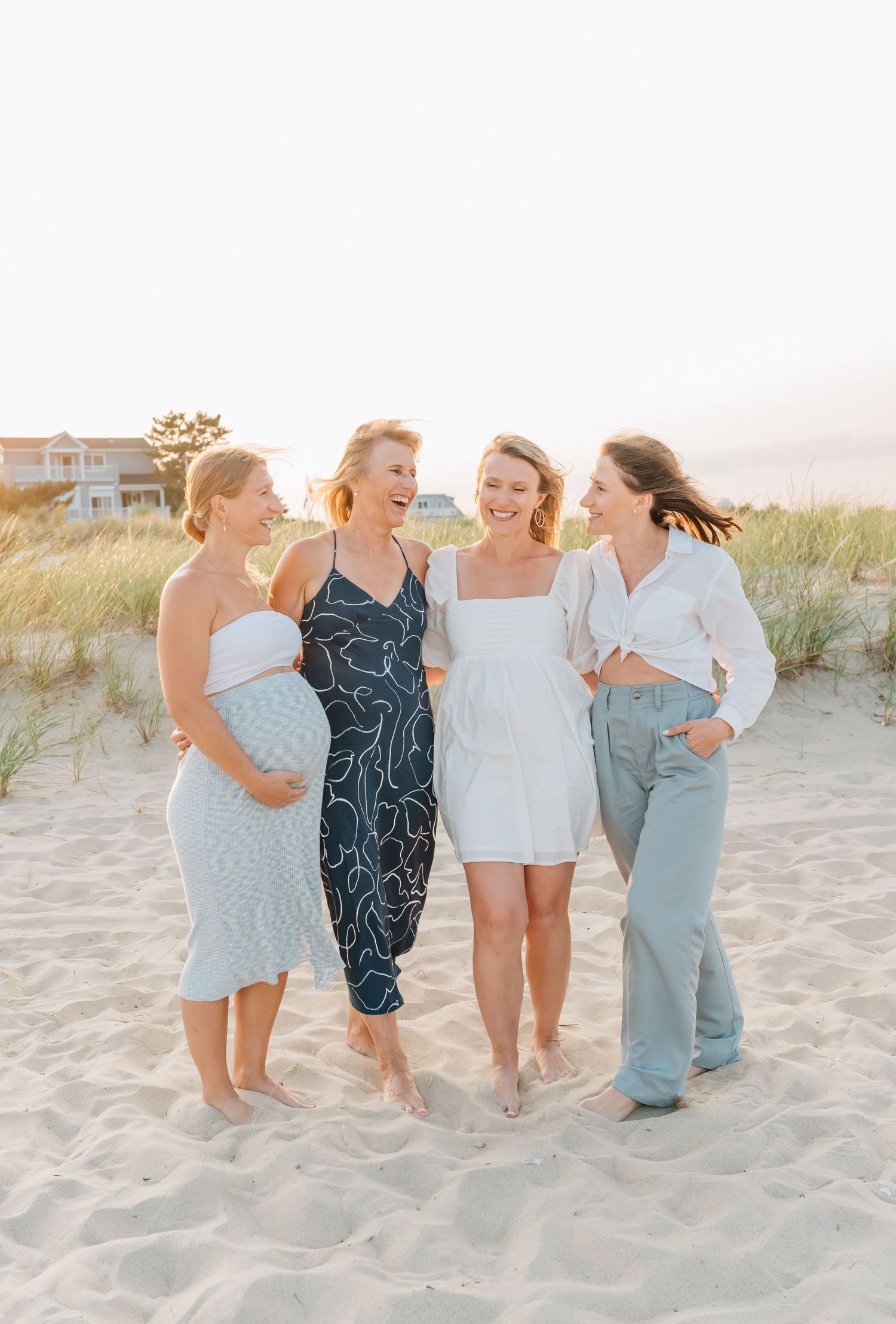 A mother and her three adult daughters have arms around each other while laughing during their extended family photo session.