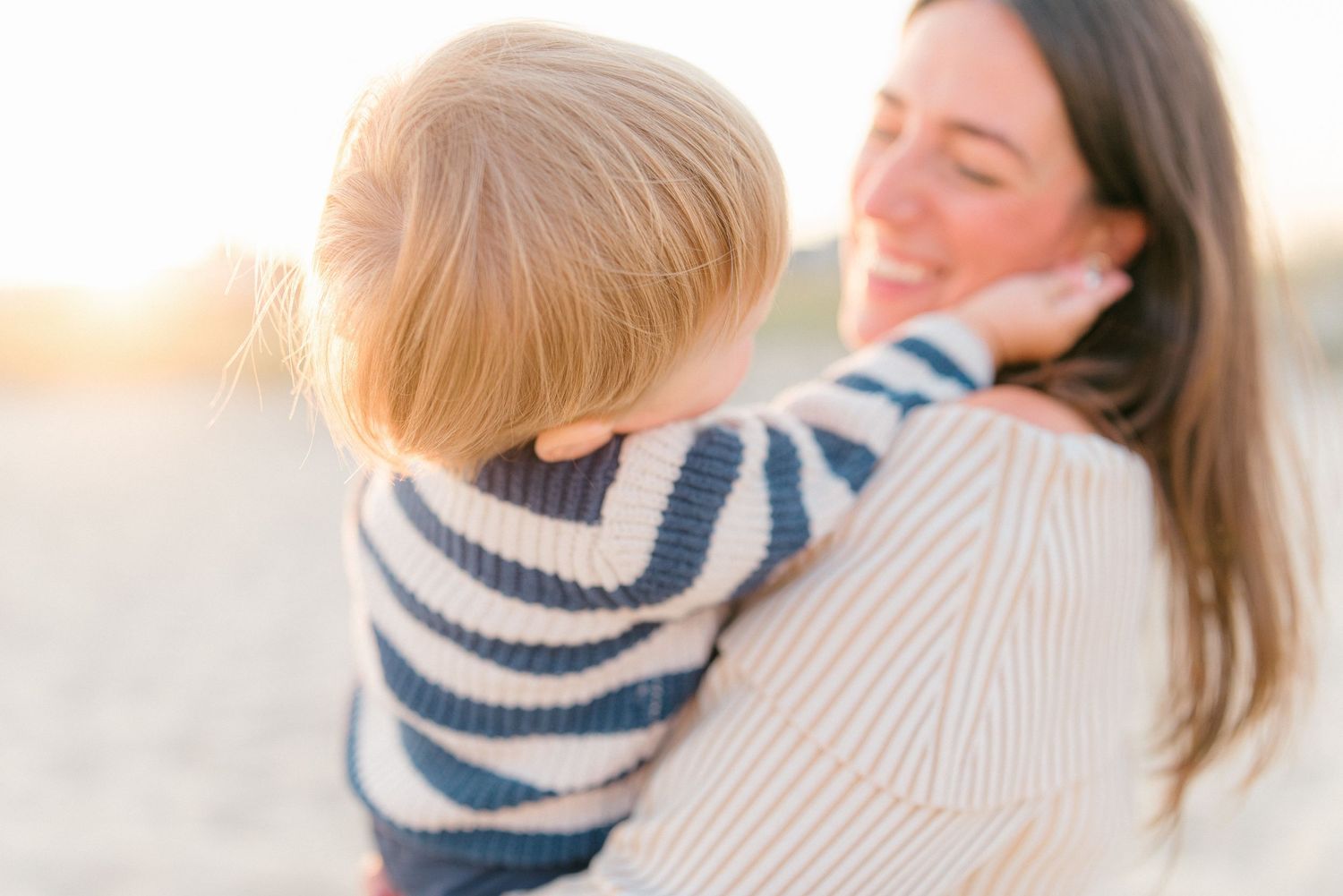 A young boy in a stripped white and blue sweater plays with his mother's ear.
