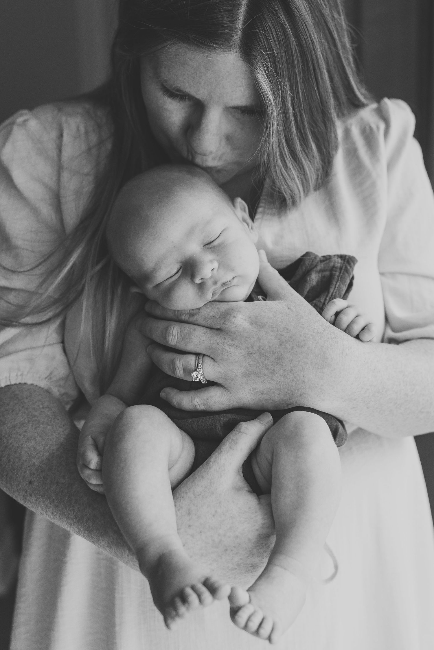 Mother holding newborn close, smiling gently during lifestyle session in Point Pleasant, New Jersey.