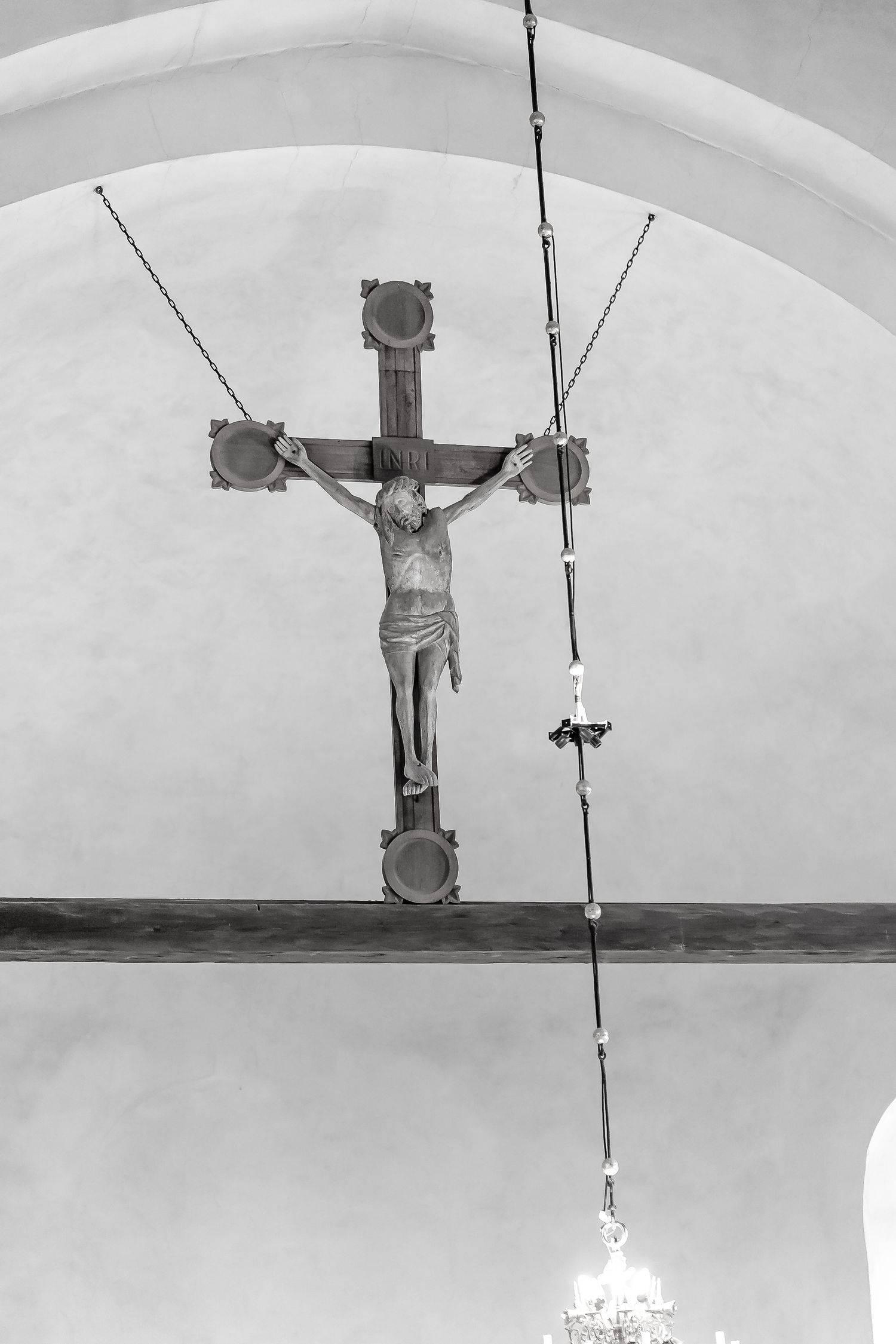 Black and white photo of a crucifix mounted above the altar in a church with an arched ceiling.