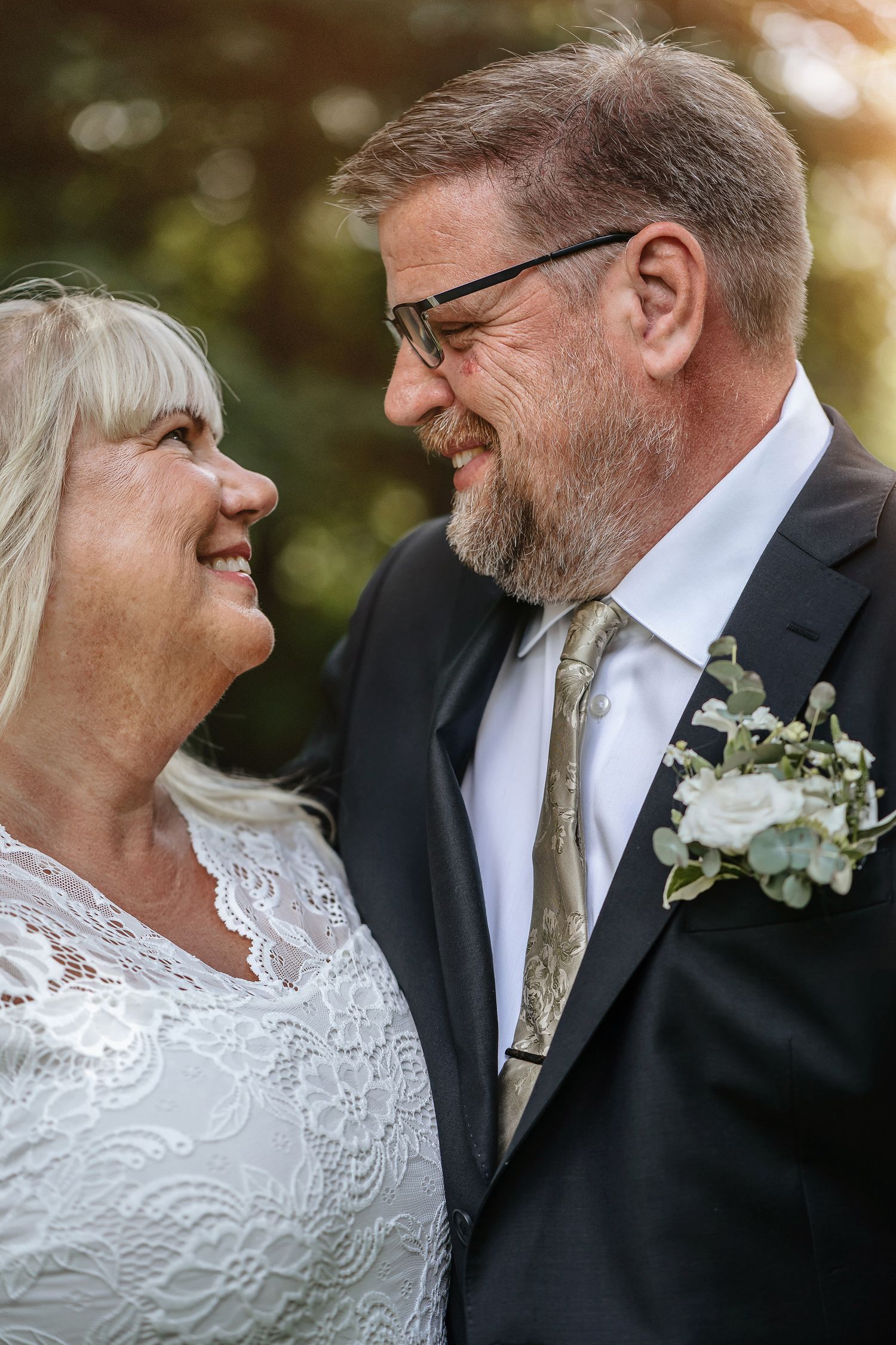 Brudparet Anna och Stefan tittar leende på varandra under porträttfotograferingen i slottsparken på Rånäs Slott.