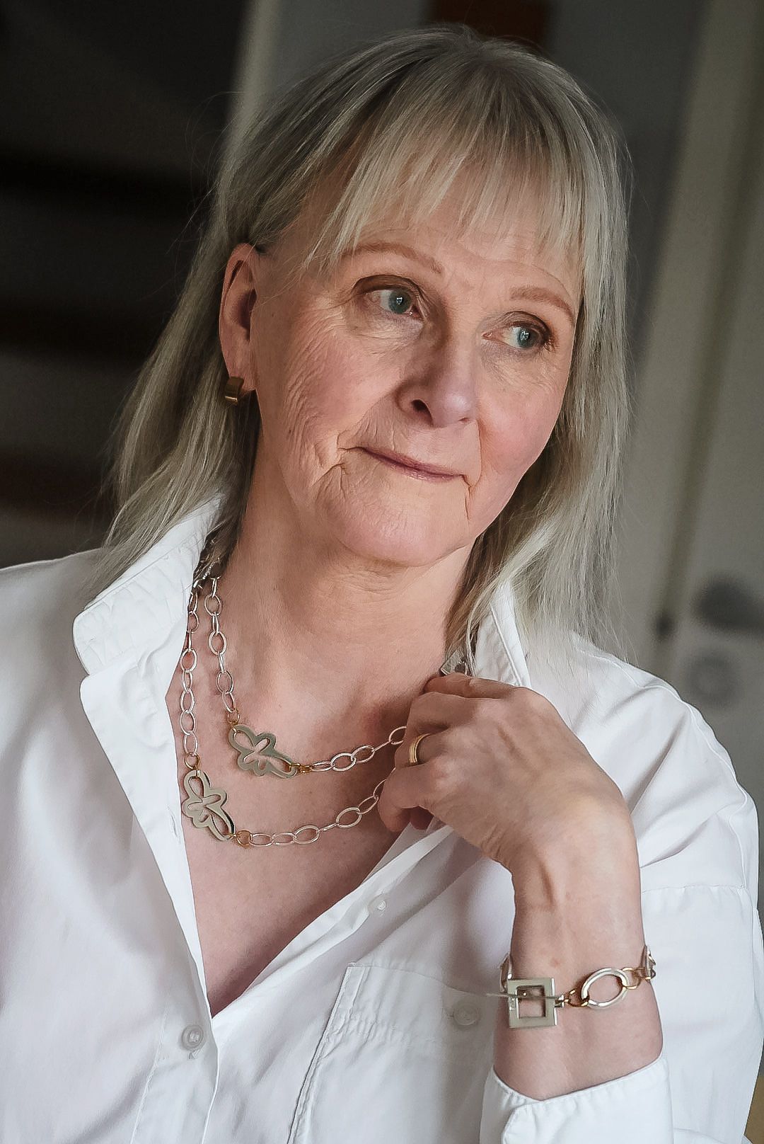 Kvinna i vit skjorta med handgjort silverhalsband i mjukt naturligt ljus.