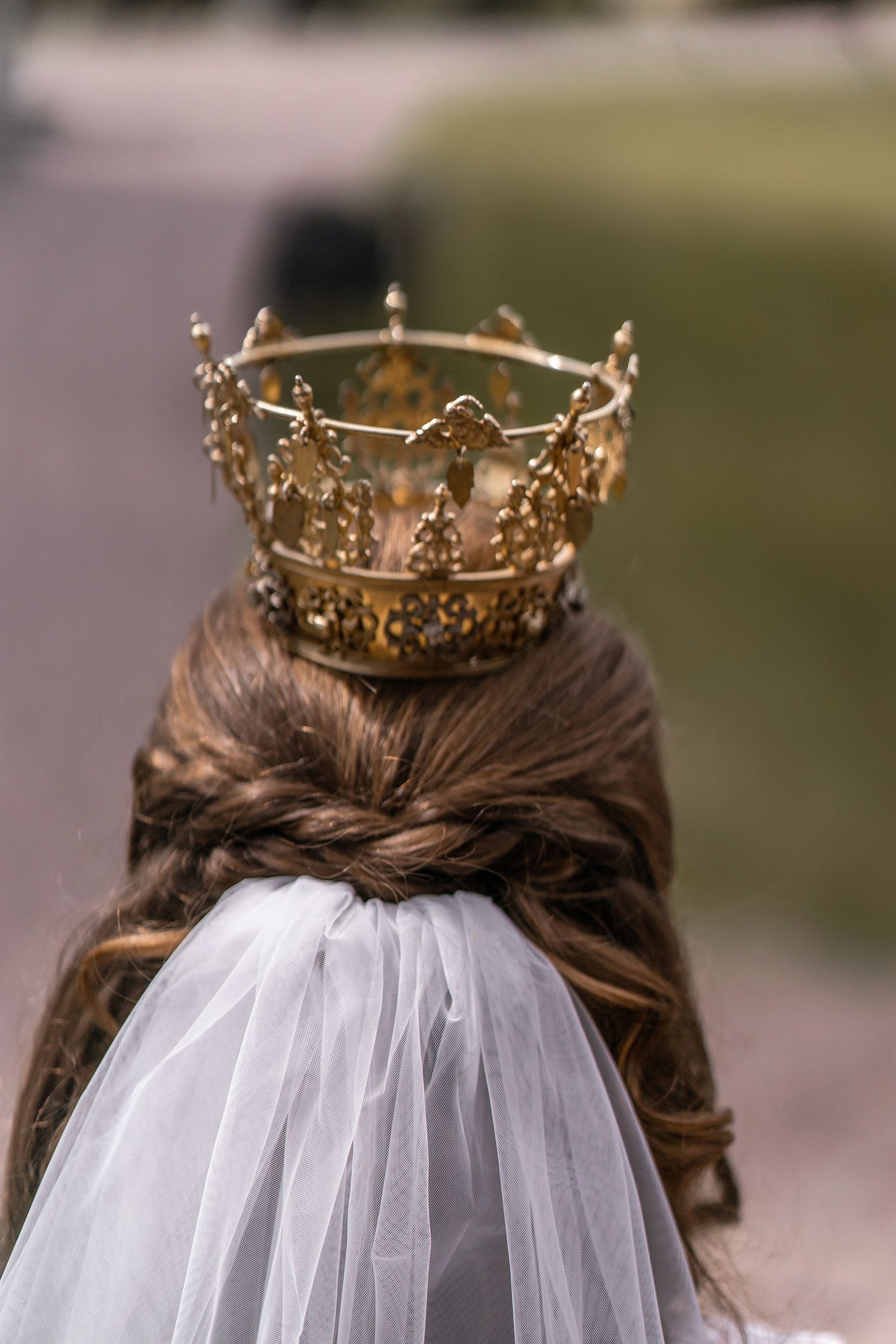 Back view of a bride wearing an ornate gold crown over a braided updo with a white veil.