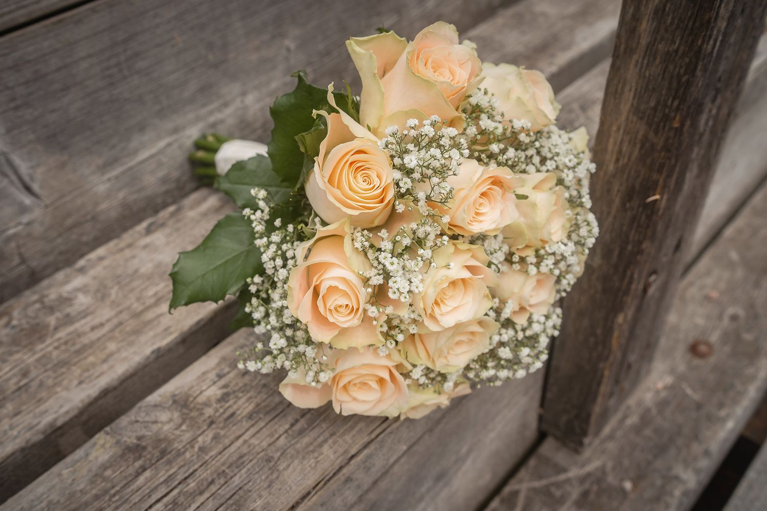 Elegant bridal bouquet of cream roses and baby's breath resting on a rustic wooden bench.