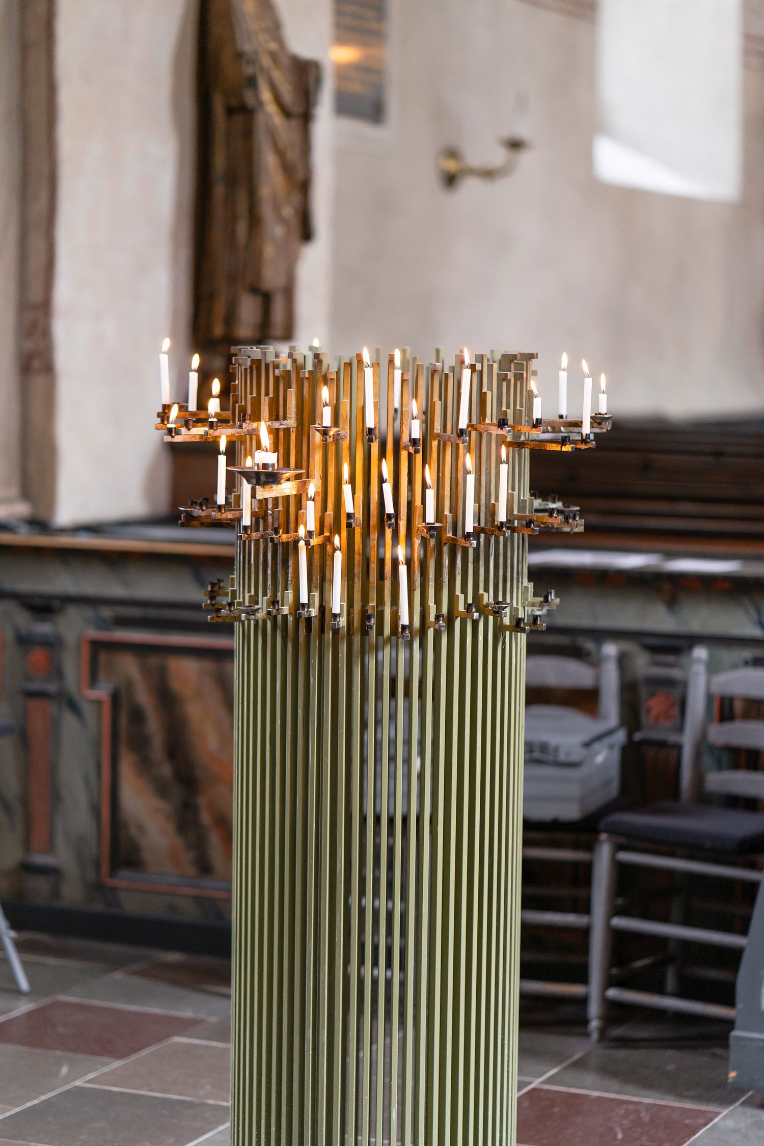 Golden candelabra with lit candles atop a tall cylindrical brass pillar inside a historic church interior.