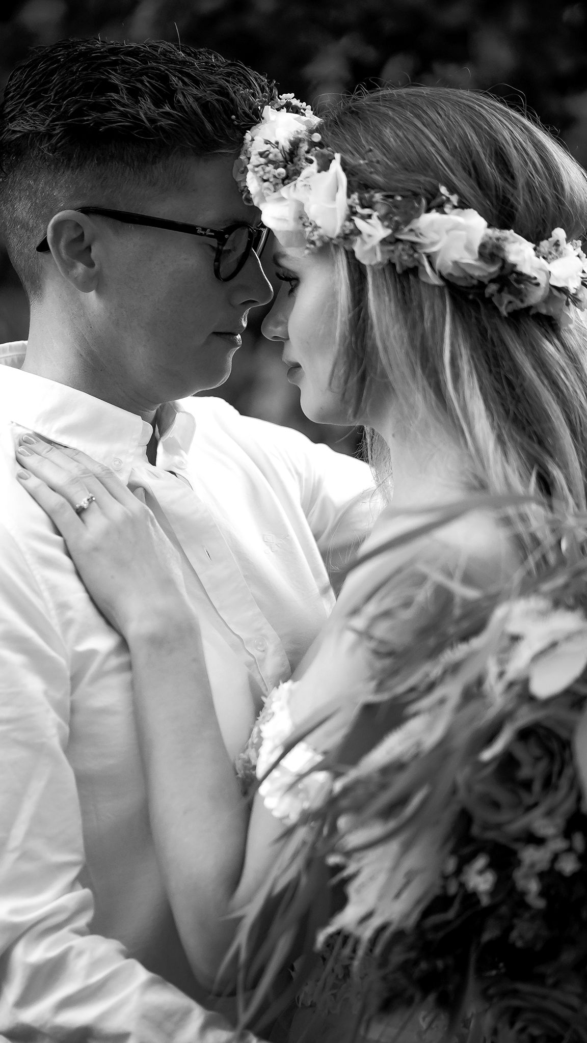 Black and white photo of a couple in an intimate moment, bride wearing a floral crown and groom in glasses.