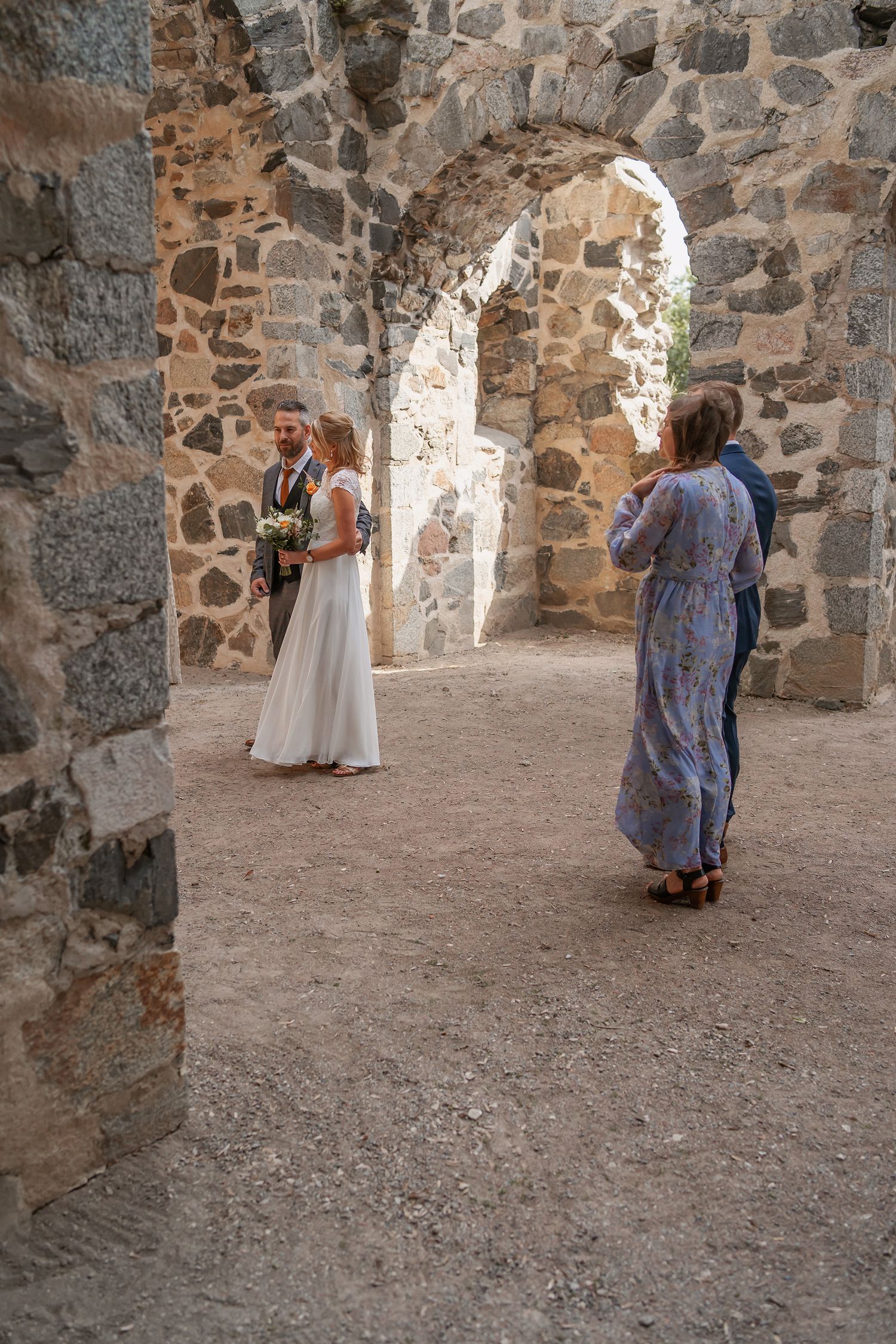Wedding photographer captures bride and groom posing under stone archway in ancient ruins venue.