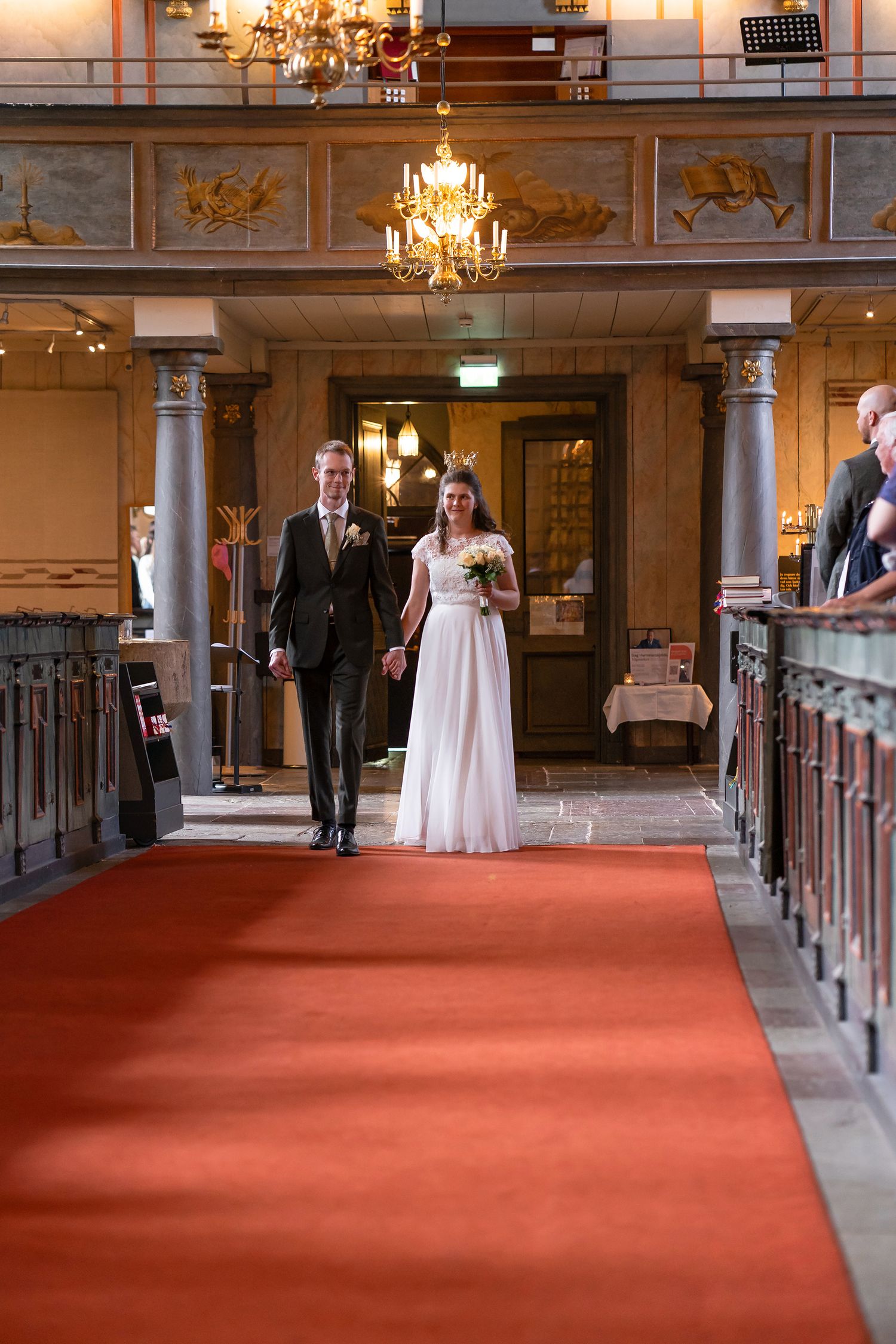 Bride and groom walking down red carpet aisle in elegant church during wedding ceremony.