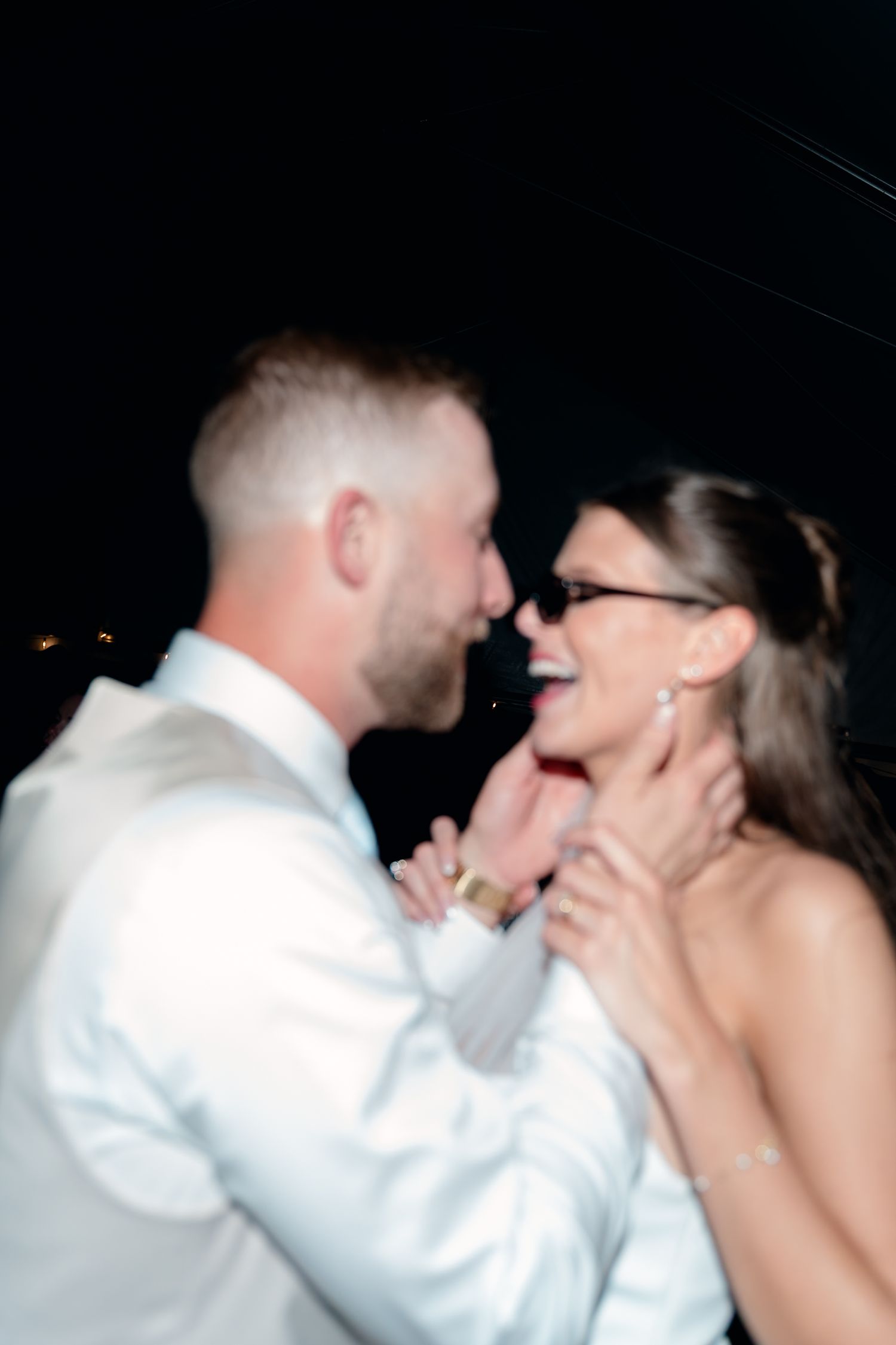 Blurred romantic moment of bride and groom laughing together closely during outdoor nighttime wedding.