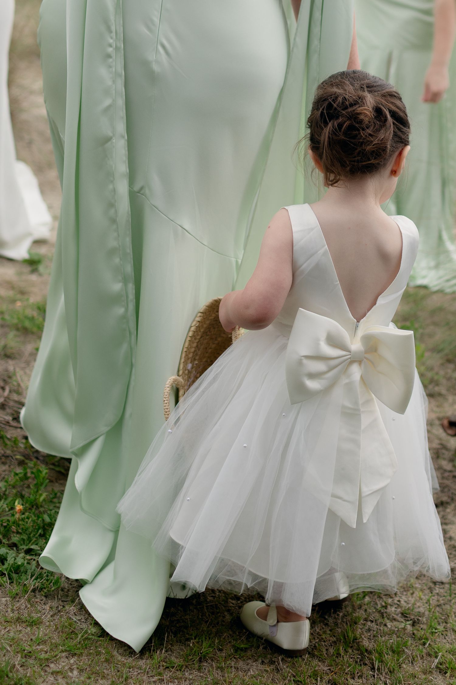 Young flower girl in white dress with large bow walking alongside bridesmaids in mint green gowns.