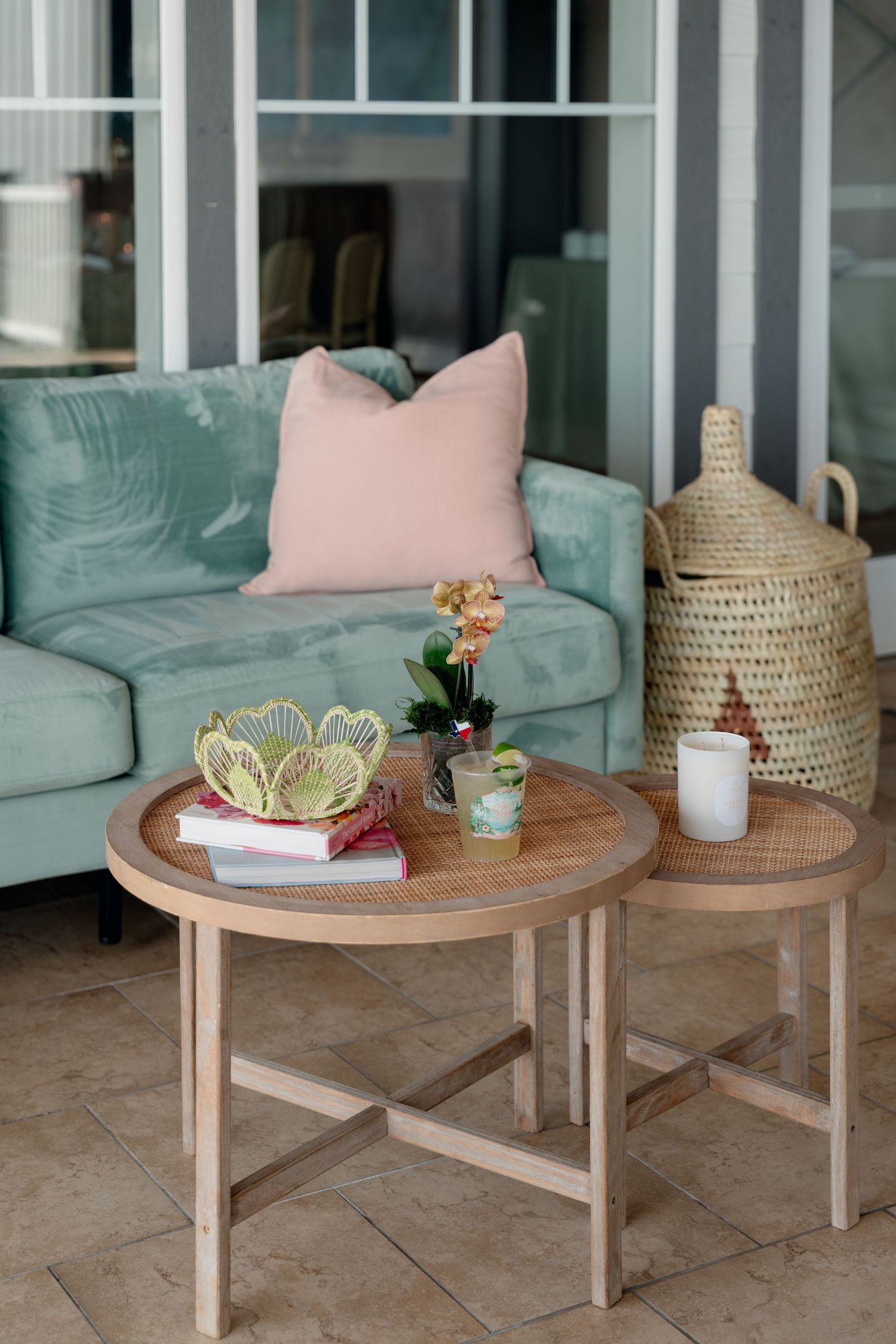 Coastal patio with mint green sofa, pink pillow, round wood coffee tables, and wicker basket decor.