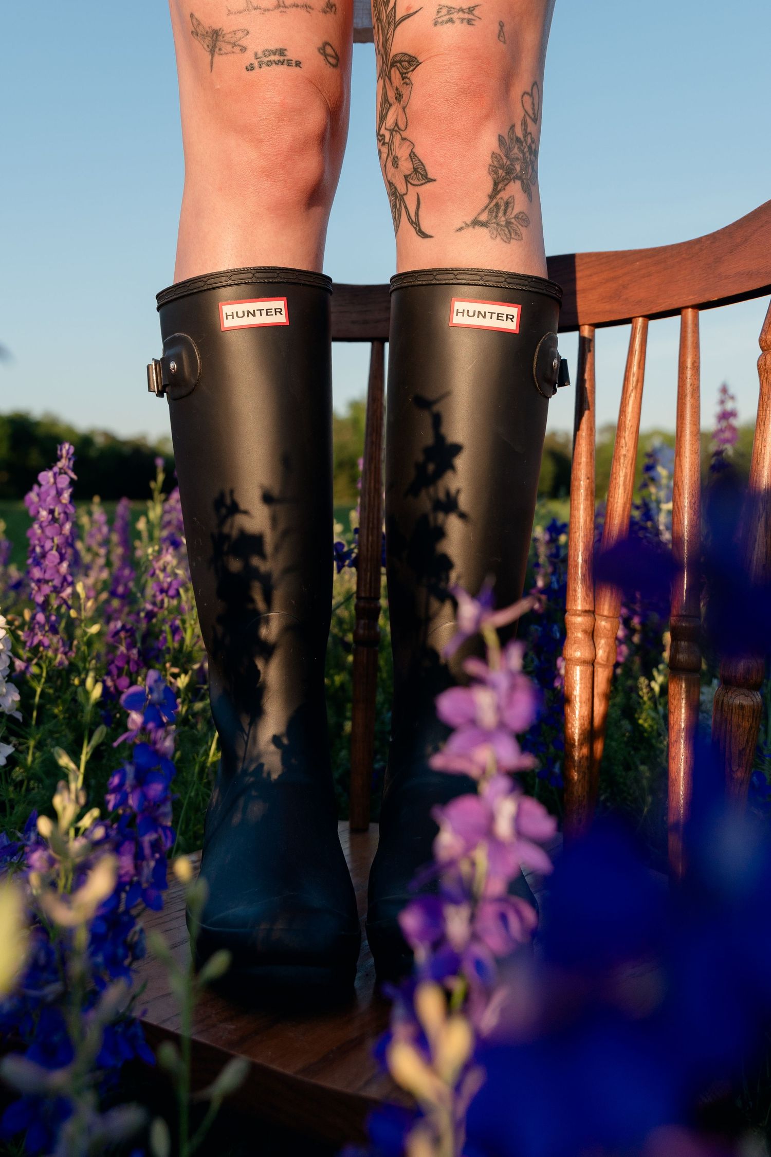 Close-up of black Hunter rain boots standing on a chair in a vibrant purple flower field.