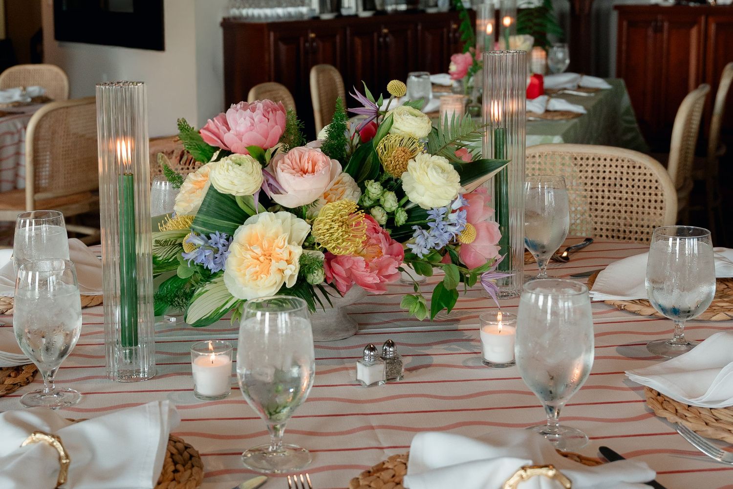 Elegant wedding reception table centerpiece with pink peonies, roses, and mixed blooms with candles.