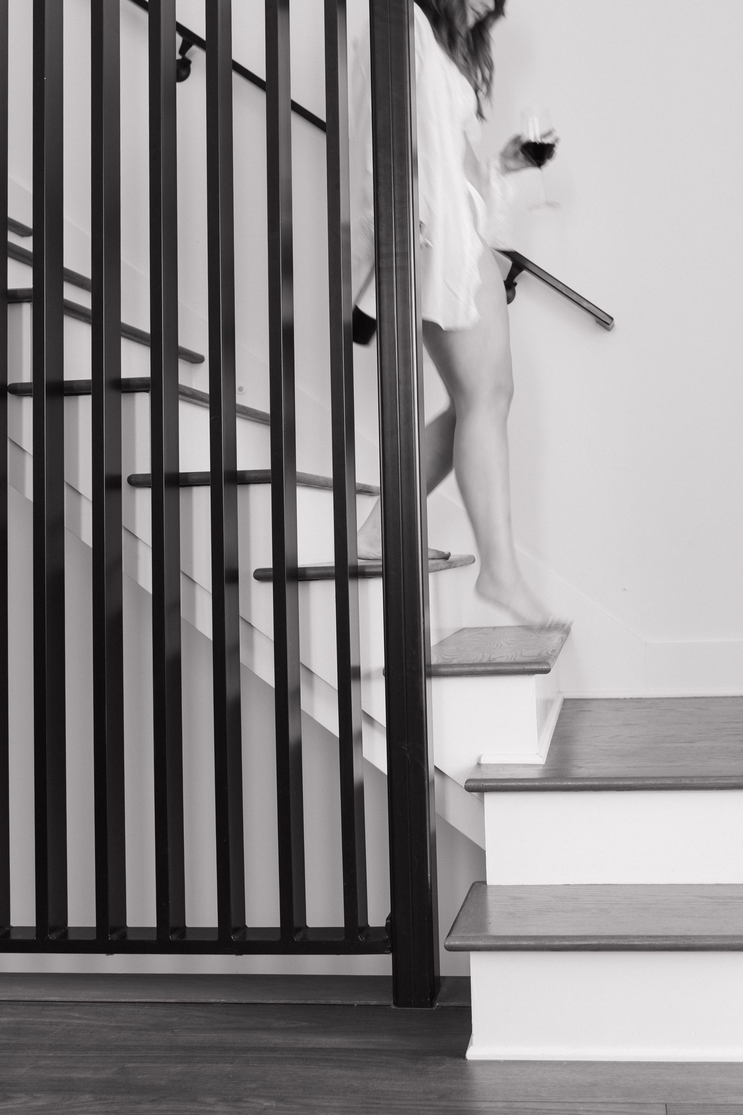 Black and white photo of woman climbing modern staircase with metal railing in bright interior.