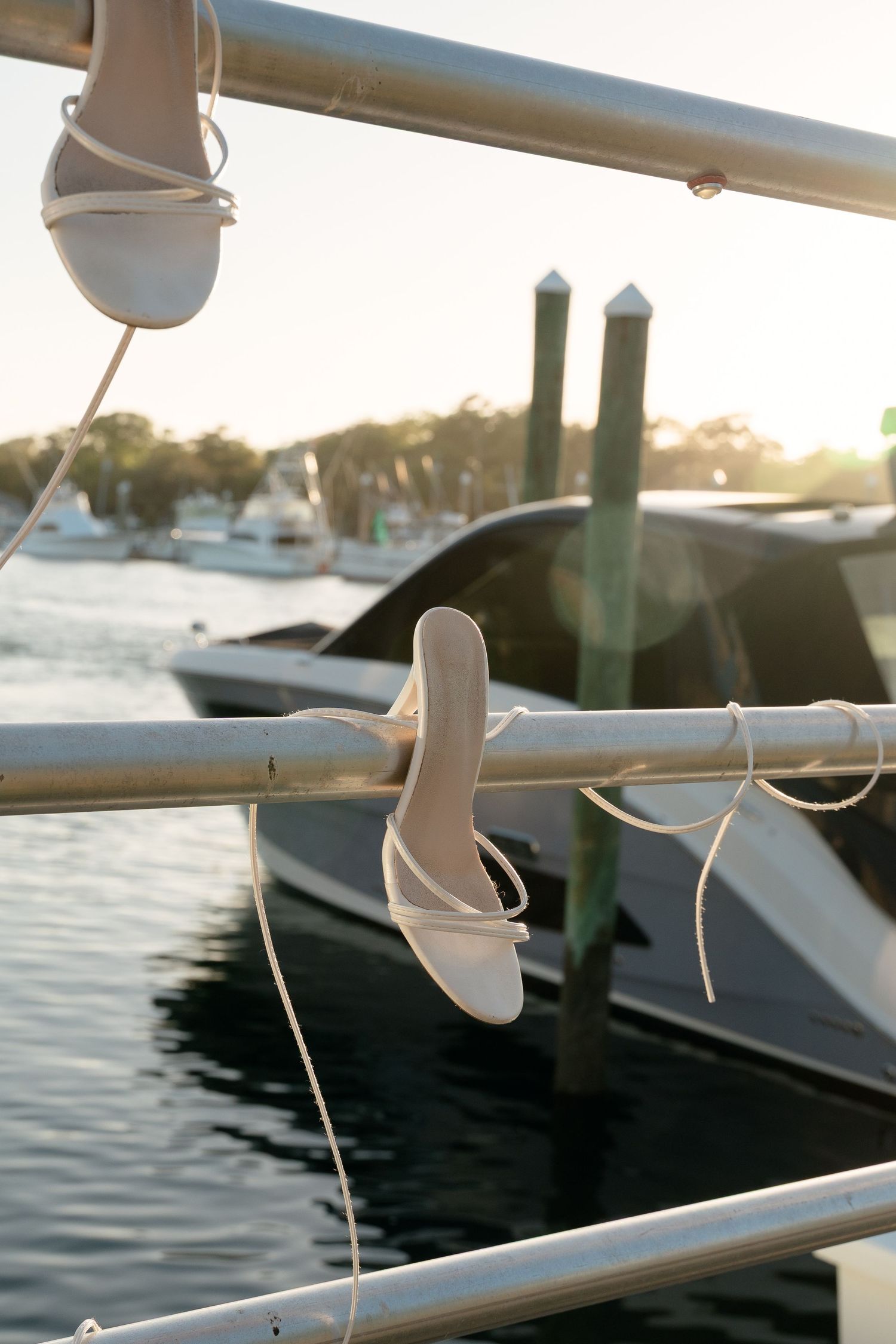 White strappy heeled sandals tied to a marina railing with boats in the background.