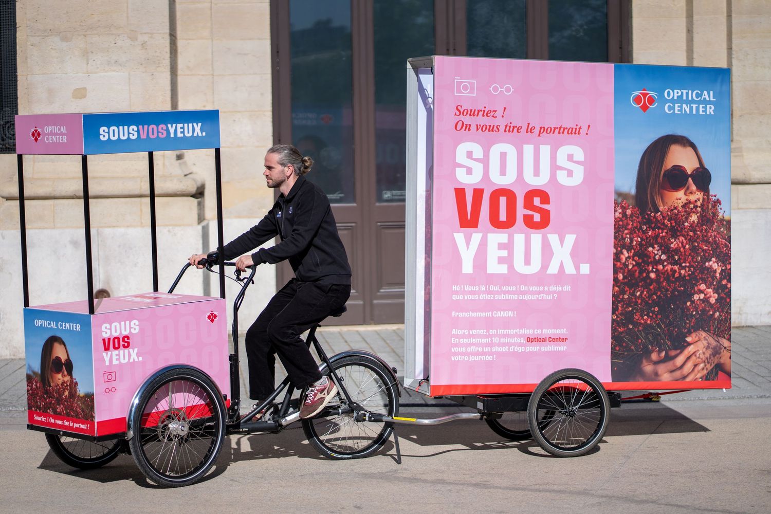 Person riding a cargo bike with Optical Center advertisement signs on streets of Paris, France.