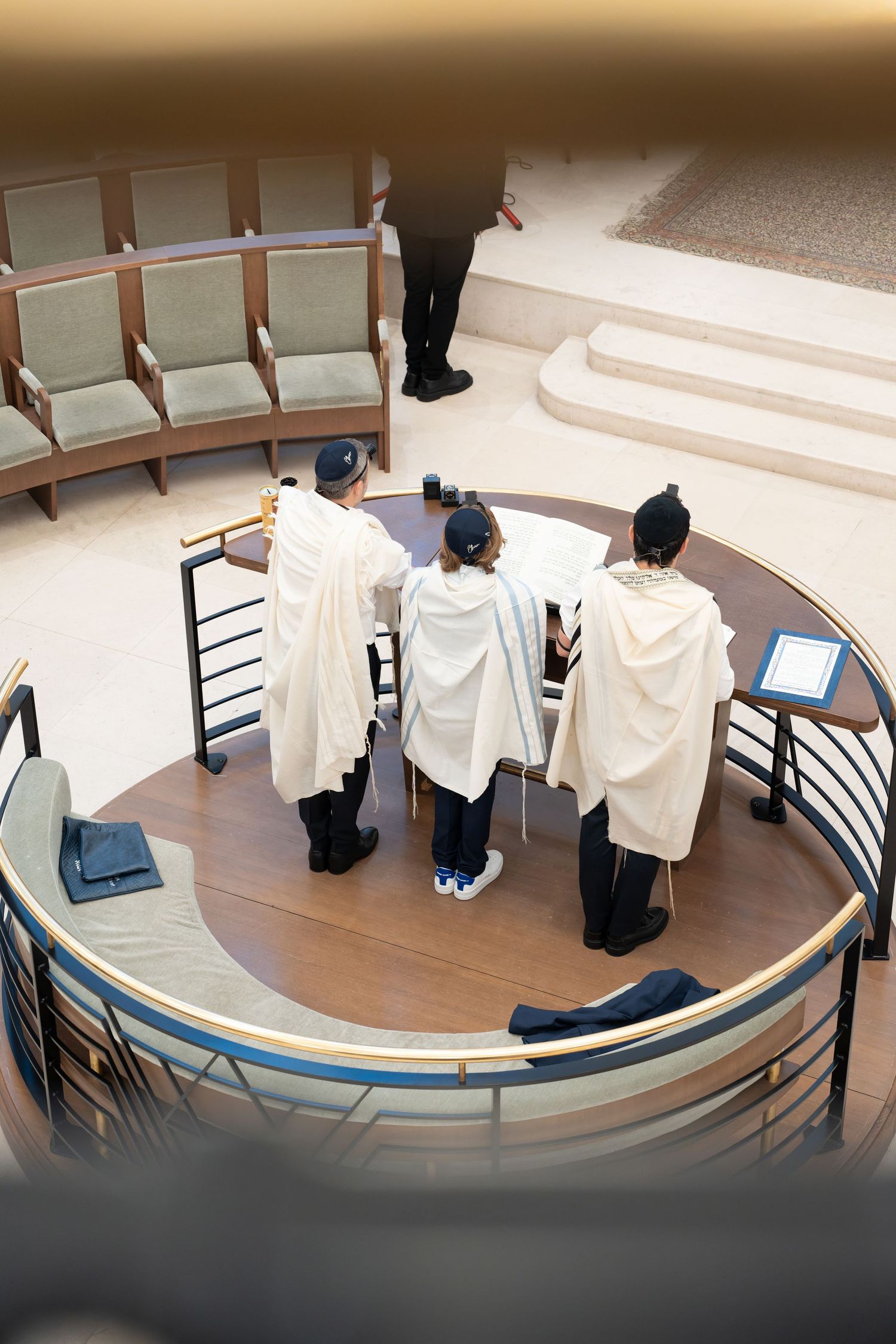 Three boys wearing white tallitot prayer shawls standing at a bimah during a Bar Mitzvah ceremony.