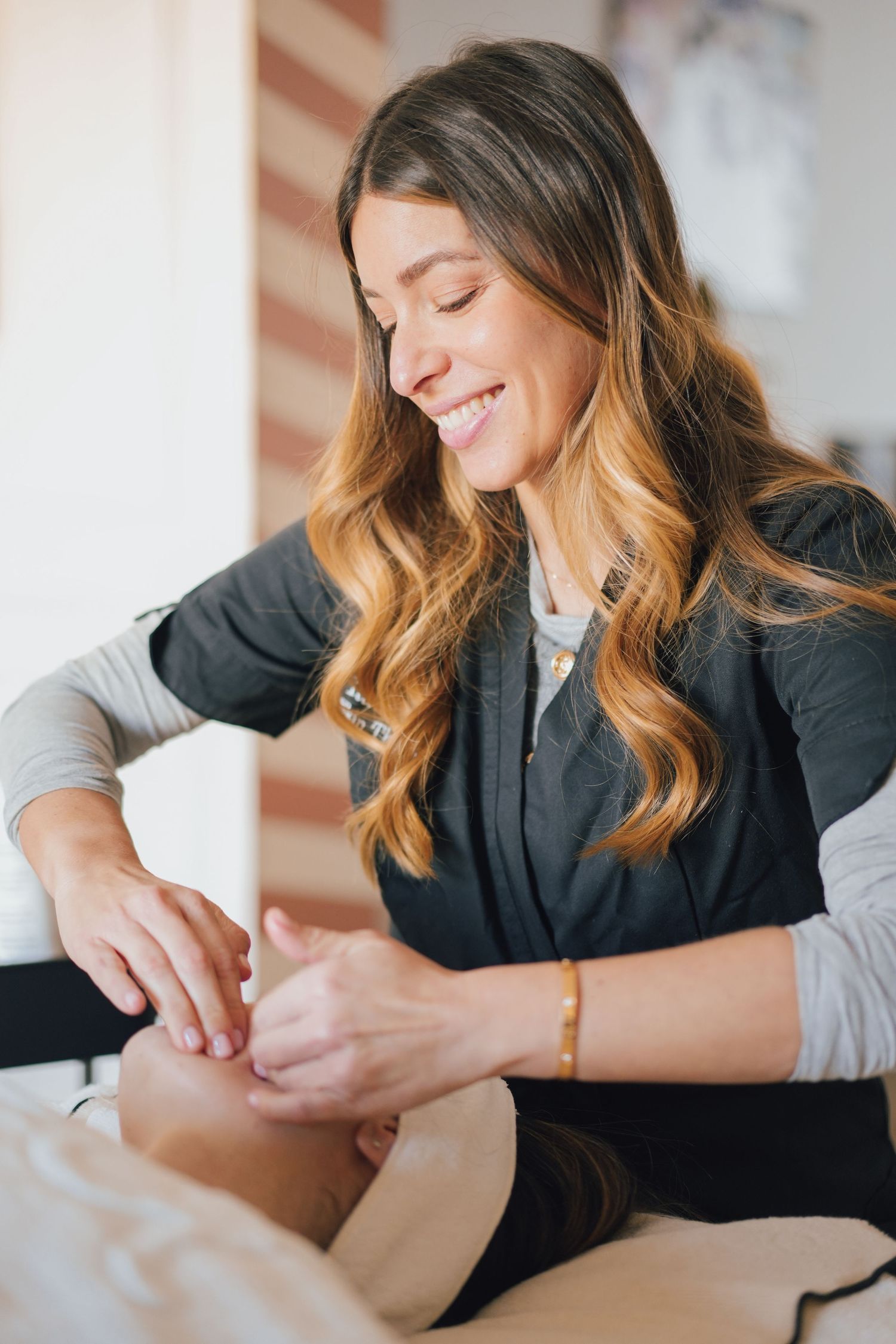 Smiling female esthetician in black uniform performing acupuncture treatment on client.