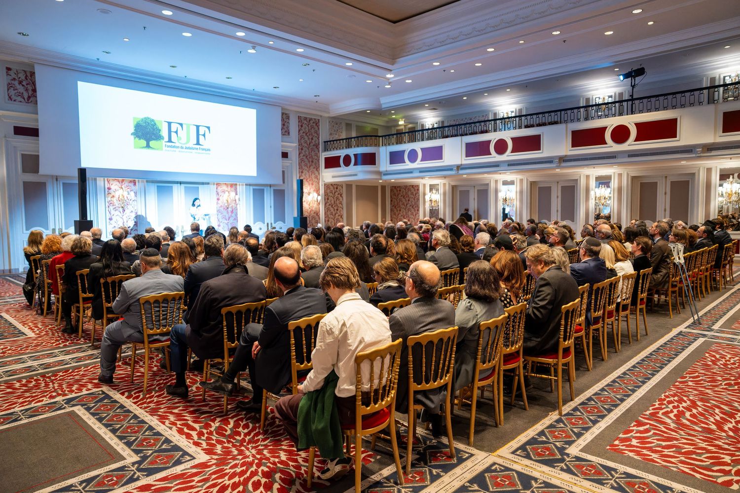Large audience seated in grand ballroom attending FJF foundation conference with green logo display.