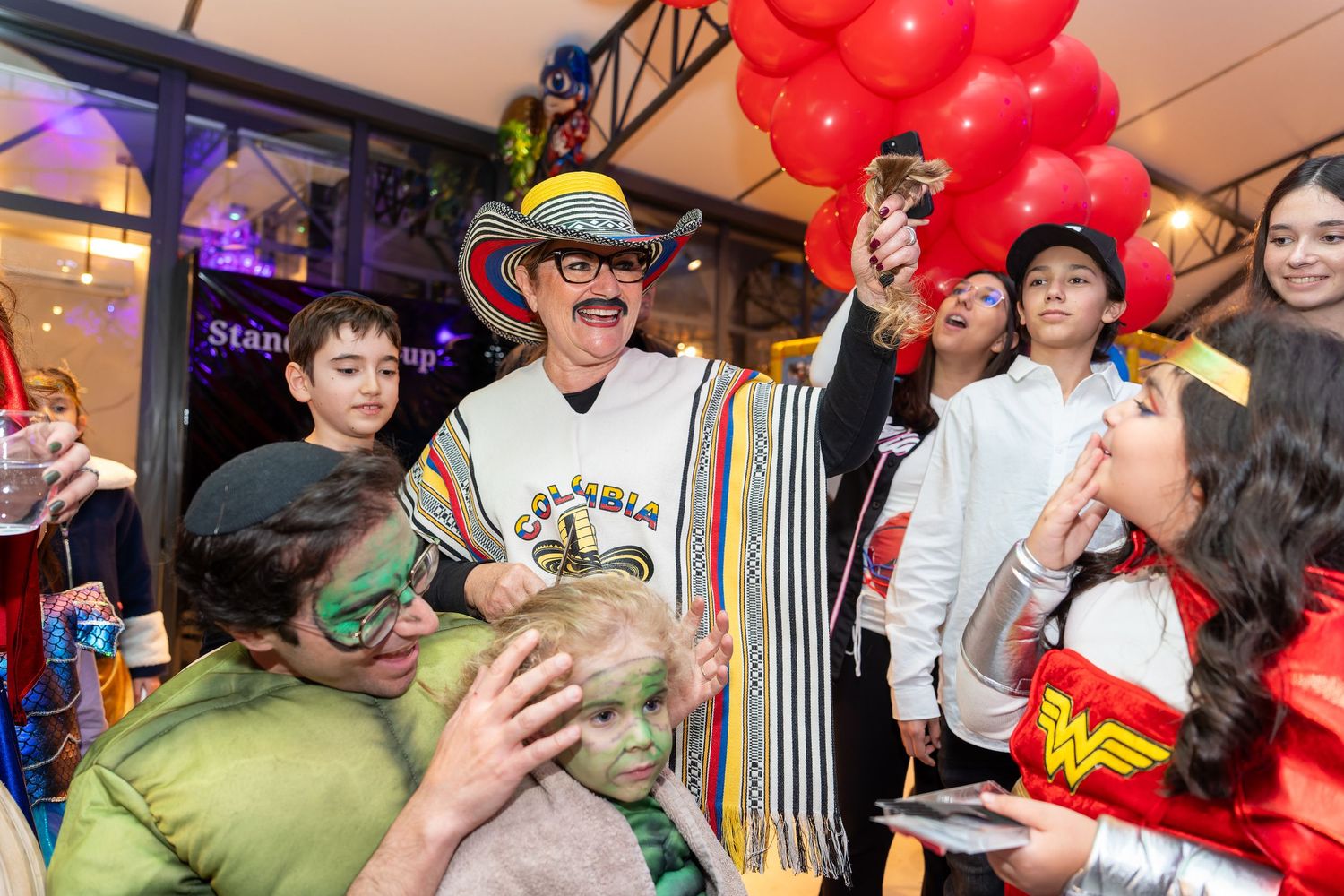 Group of people in colorful costumes celebrating at a festive party with red balloons.