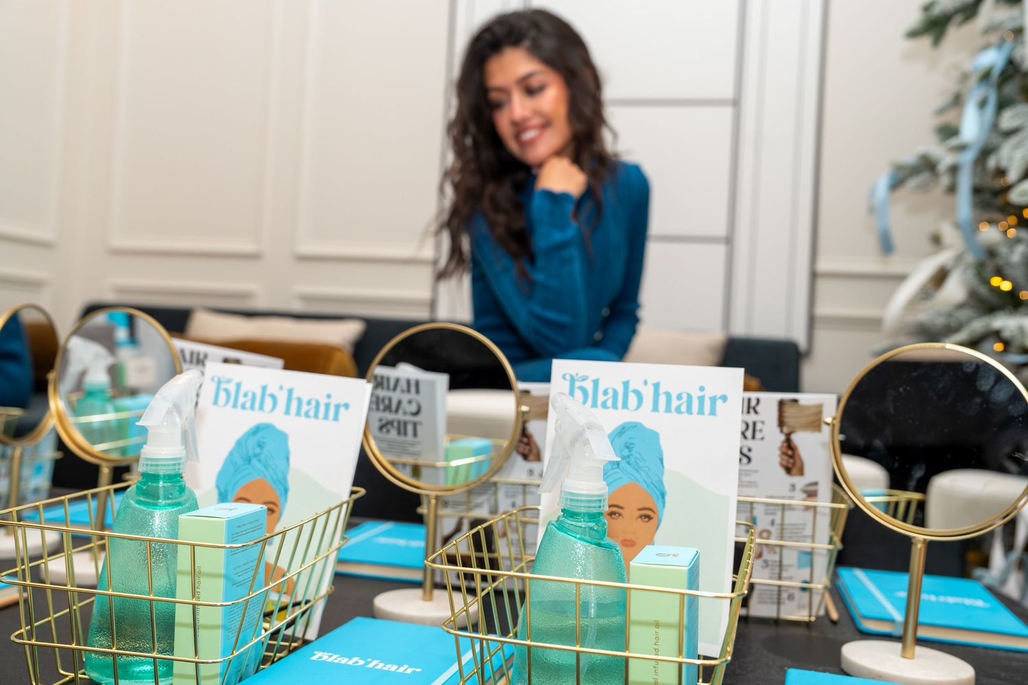 Woman smiling at Blab Hair product display with gold wire baskets at a promotional event.