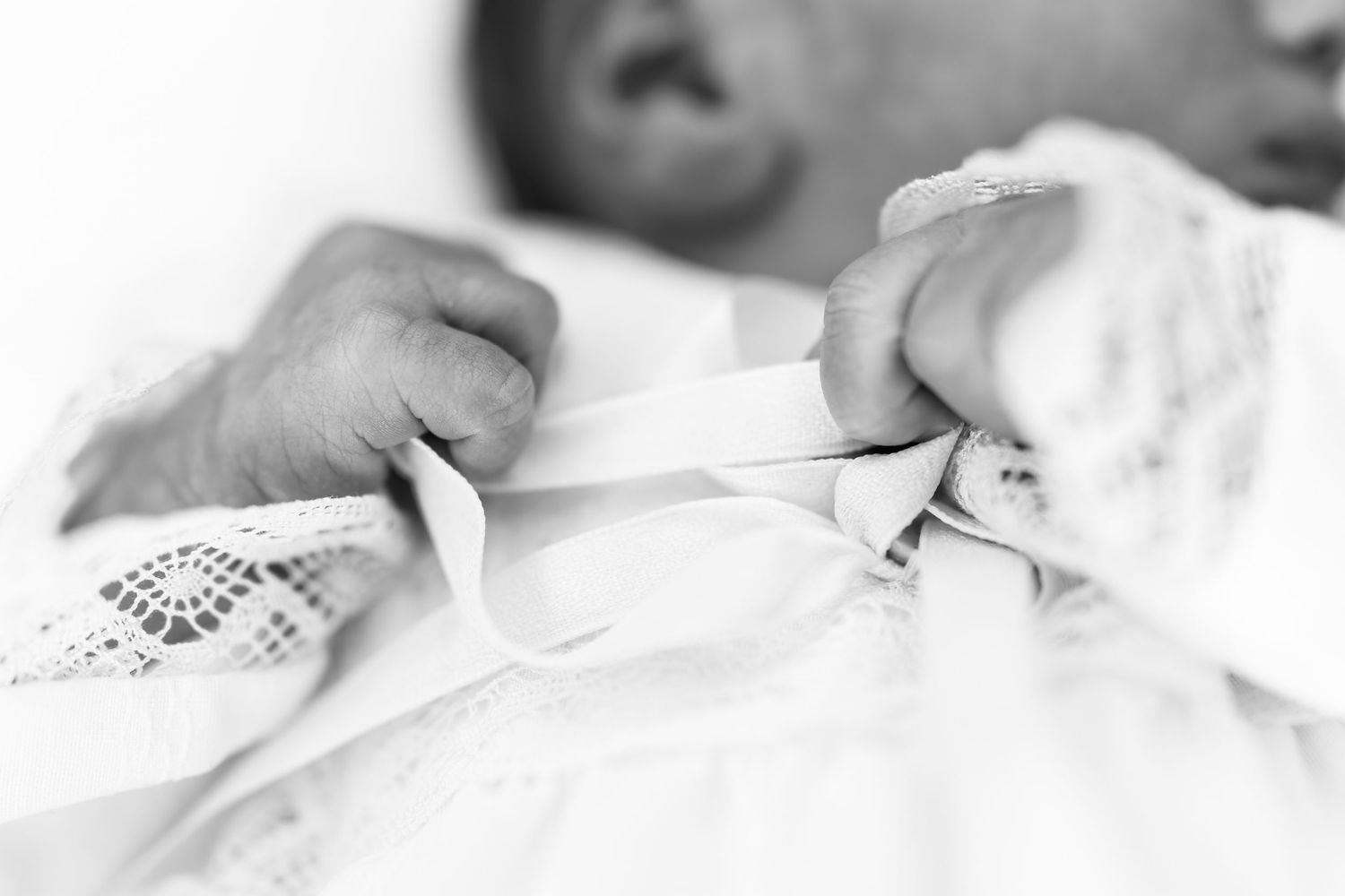Black and white photo of a newborn baby holding an adult's finger in a hospital setting.