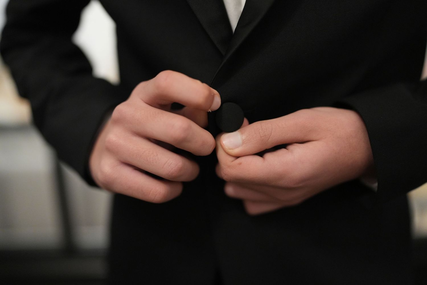 Close-up of young mans hands buttoning black suit jacket before Bar Mitzvah ceremony.