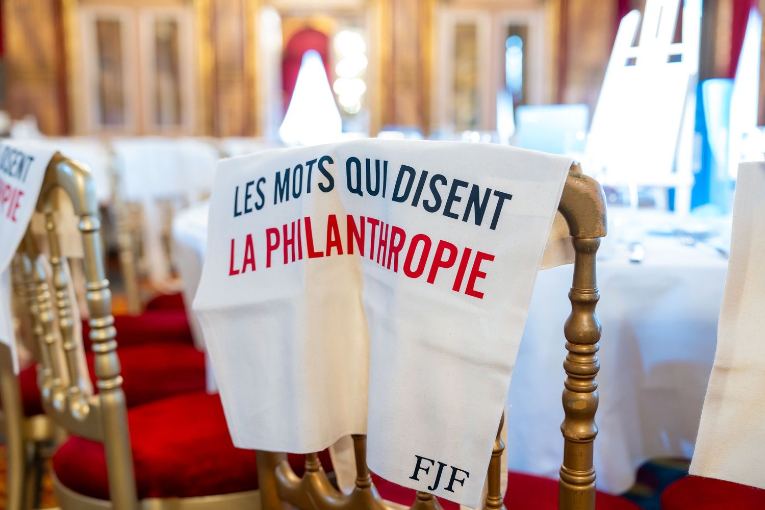 White chair covers printed with FJF philanthropy event text in ornate red and gold ballroom.