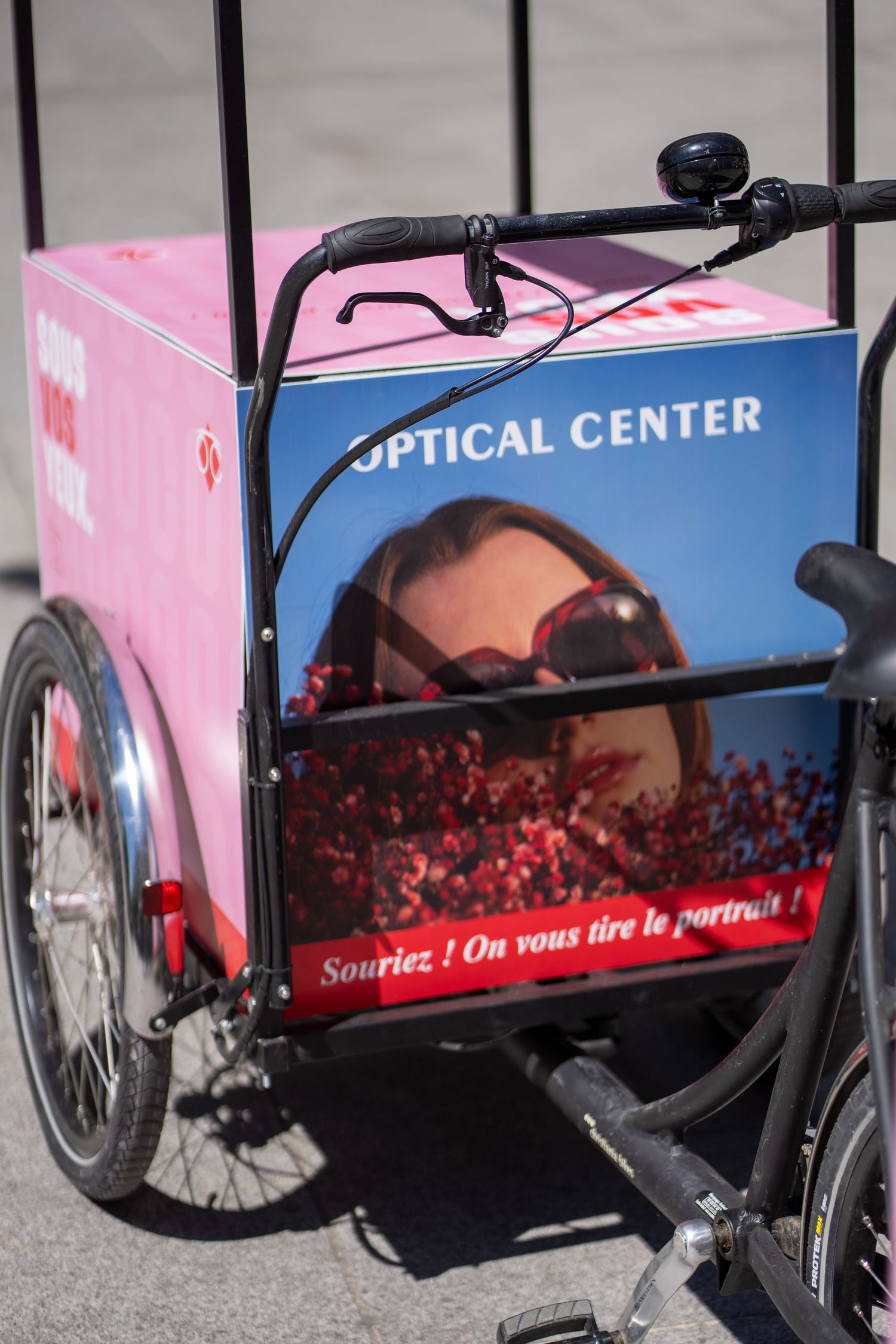 Optical Center branded cargo bike tricycle with sunglasses advertisement and French text Souriez on vous tire le portrait.