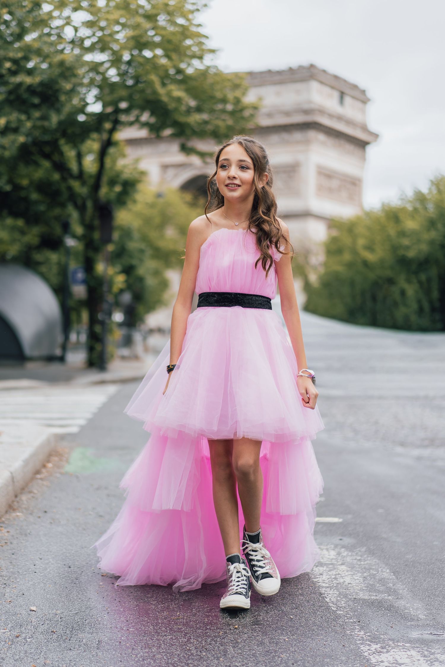 Young girl in pink tulle dress with black belt and sneakers posing near Arc de Triomphe in Paris.