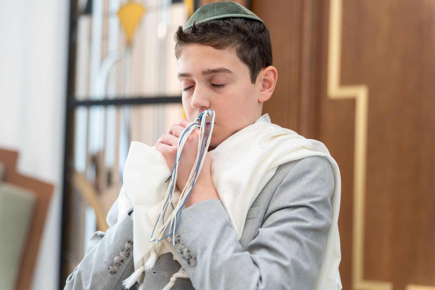 Jewish boy in kippah and tallit prays during Bar Mitzvah religious ceremony.