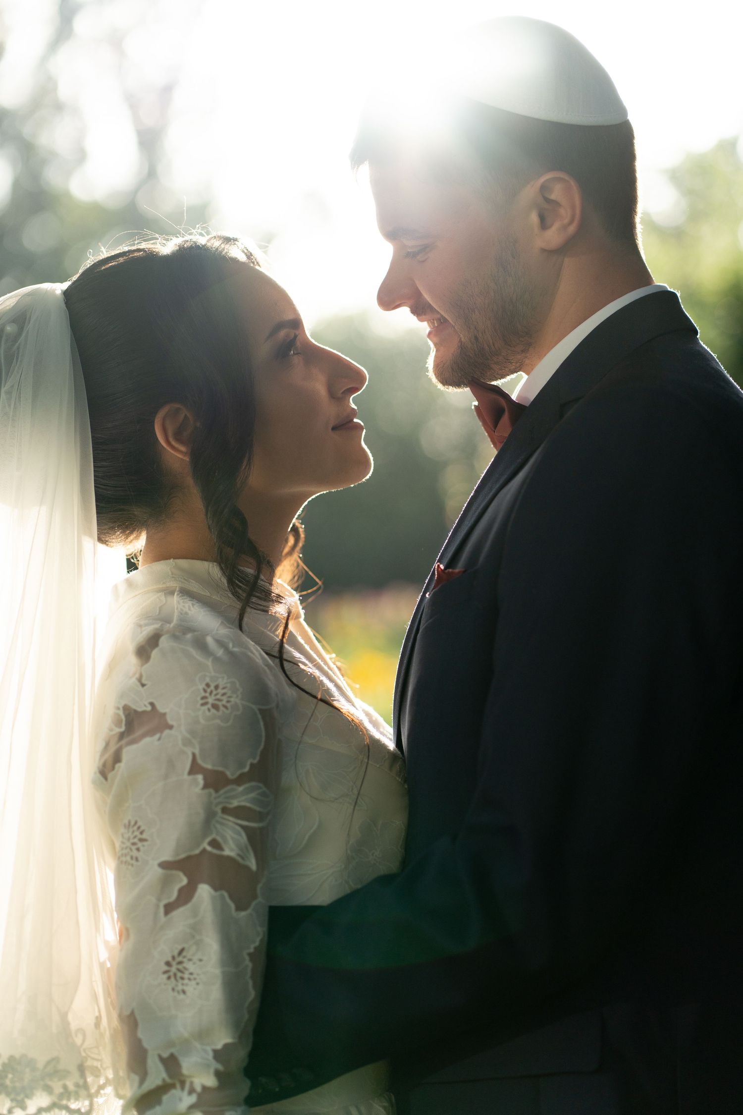 Jewish bride and groom share an intimate moment outdoors, bathed in golden sunlight during their wedding ceremony.