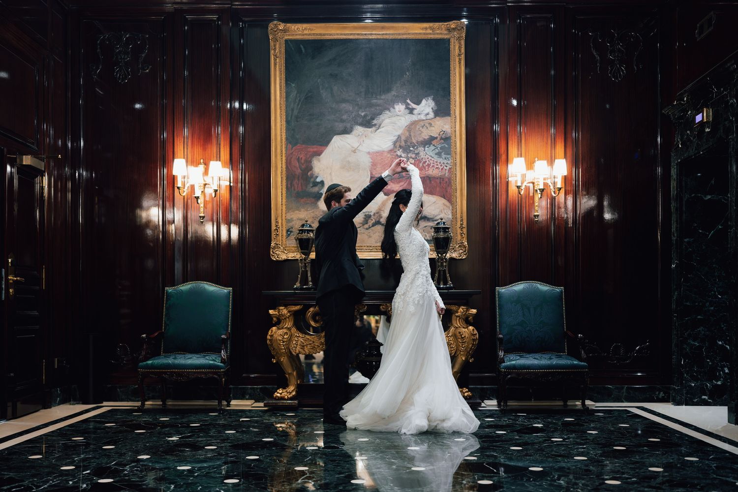Bride and groom dancing elegantly in a grand ballroom with rich wood paneling and a classic portrait painting.