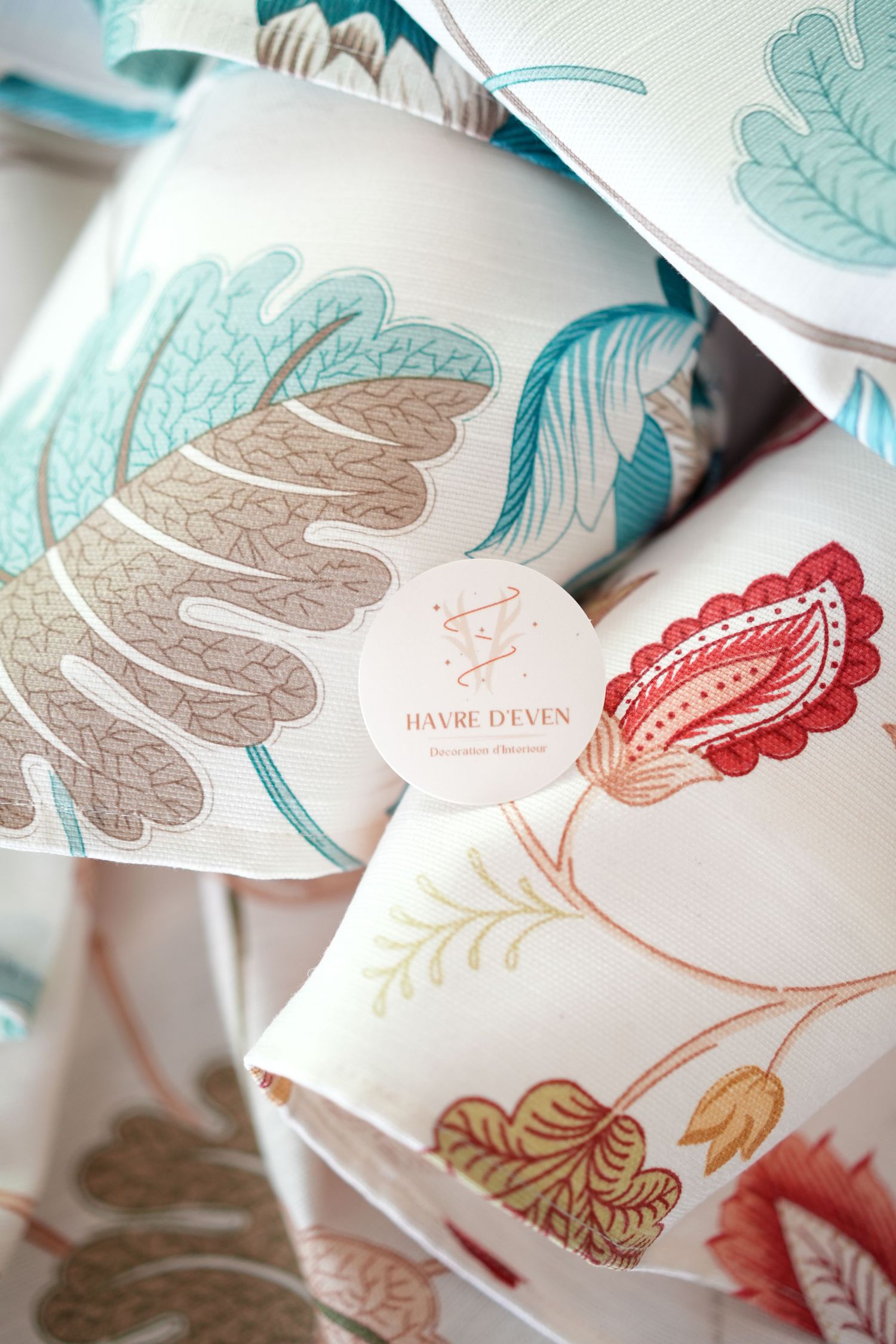 Decorative floral print cushions with Havre d'Even brand label stacked together.