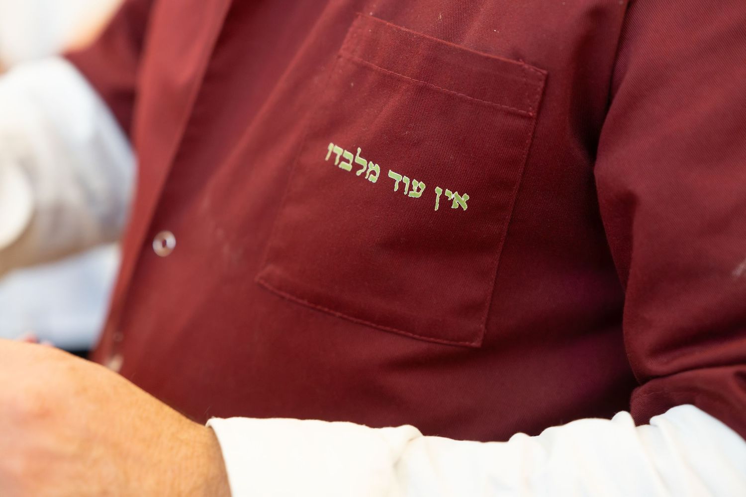 Close-up of a maroon shirt with gold Hebrew text embroidery on the chest pocket.