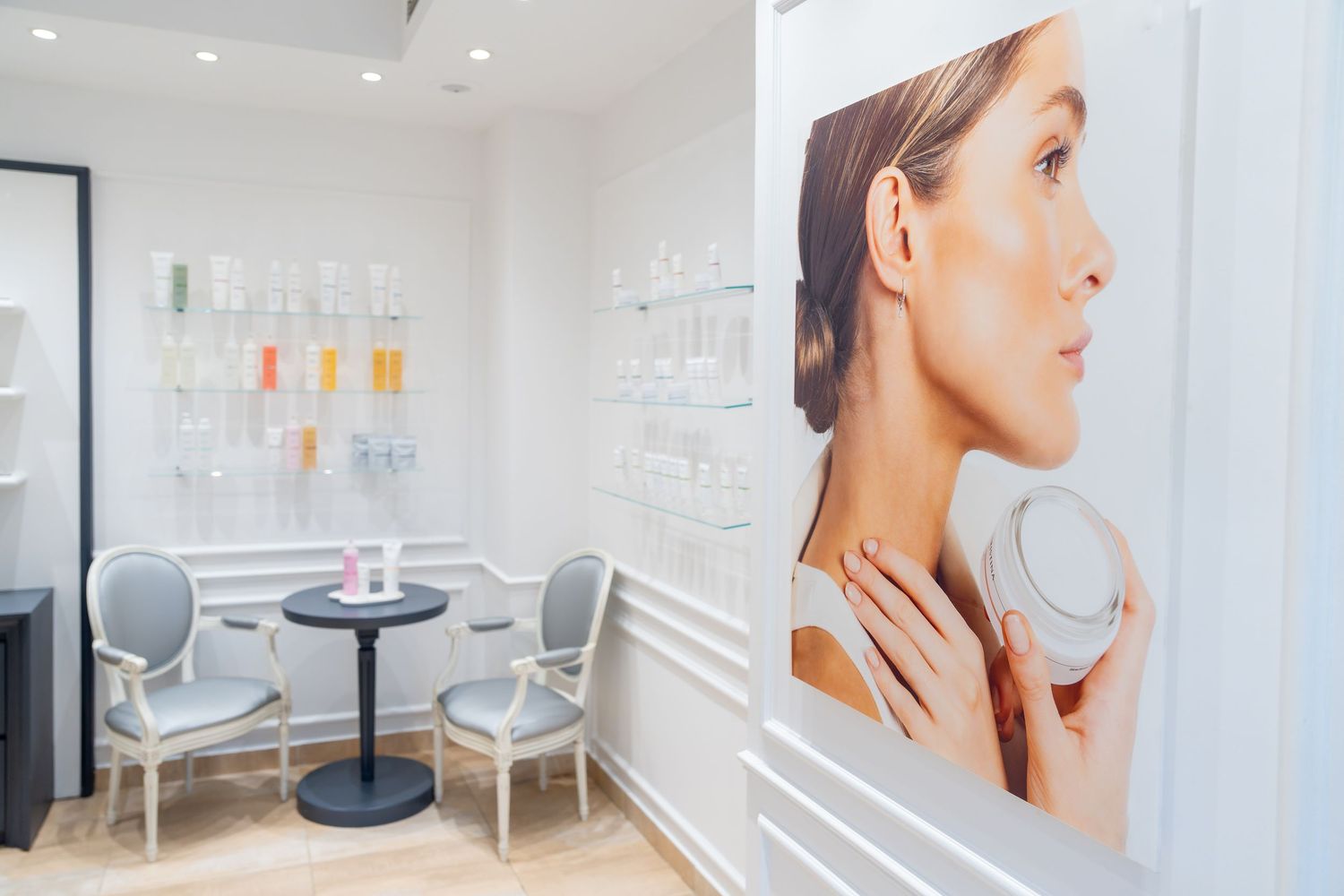 Elegant white beauty spa consultation room with large skincare advertisement and product display wall.