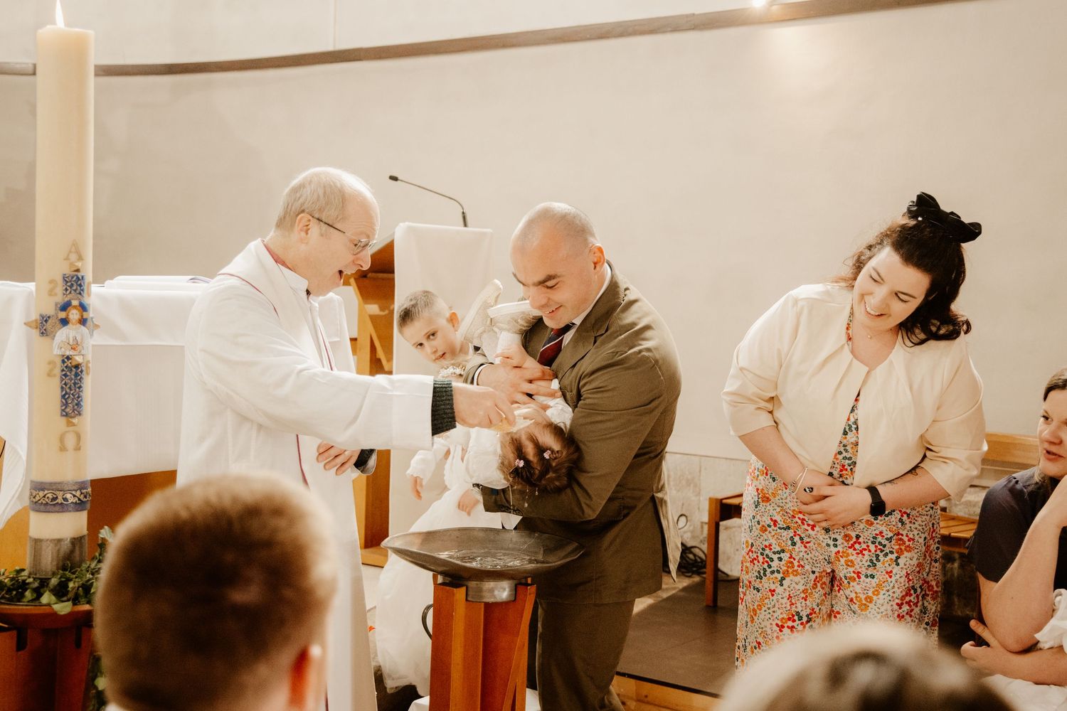 papa qui tien dans ses bras sa fille qui se fait baptiser par le prêtre lors de son baptême