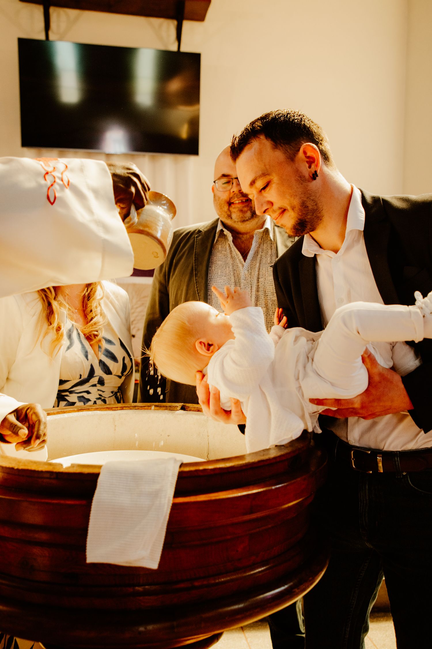 parrain qui porte son neveux dans les bras pendant qu'il se fait baptiser