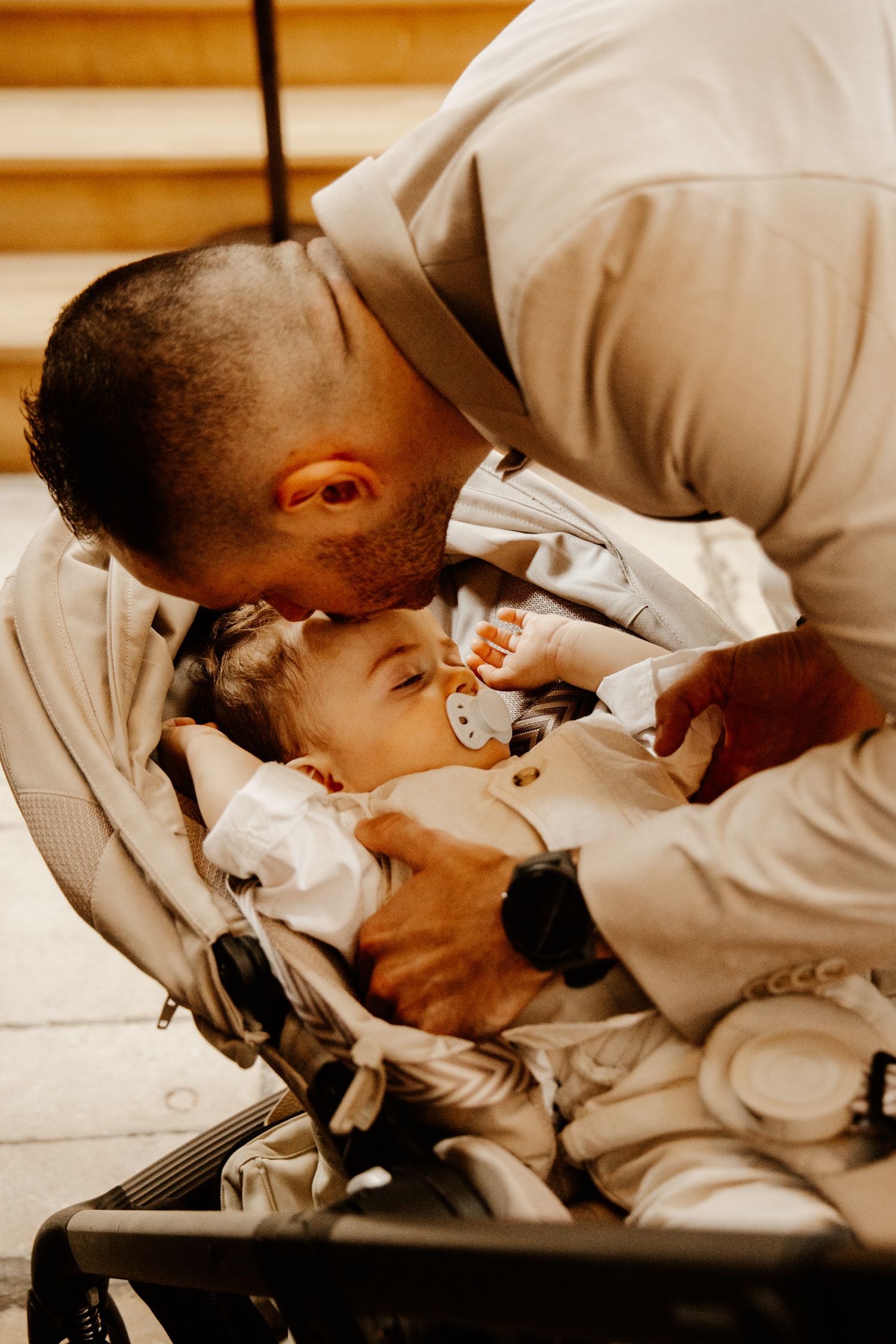 papa qui embrasse son bébé entrain de dormir dans la poussette lors de son baptême