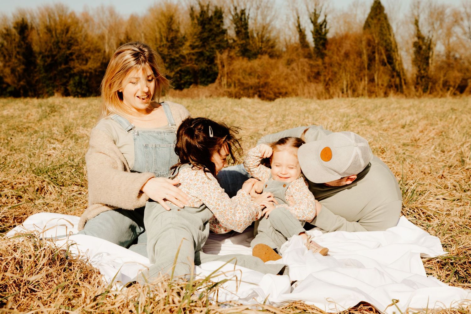 famille qui se fait un câlin dans un champs en rigolant pendant une séance photo famille en extérieur