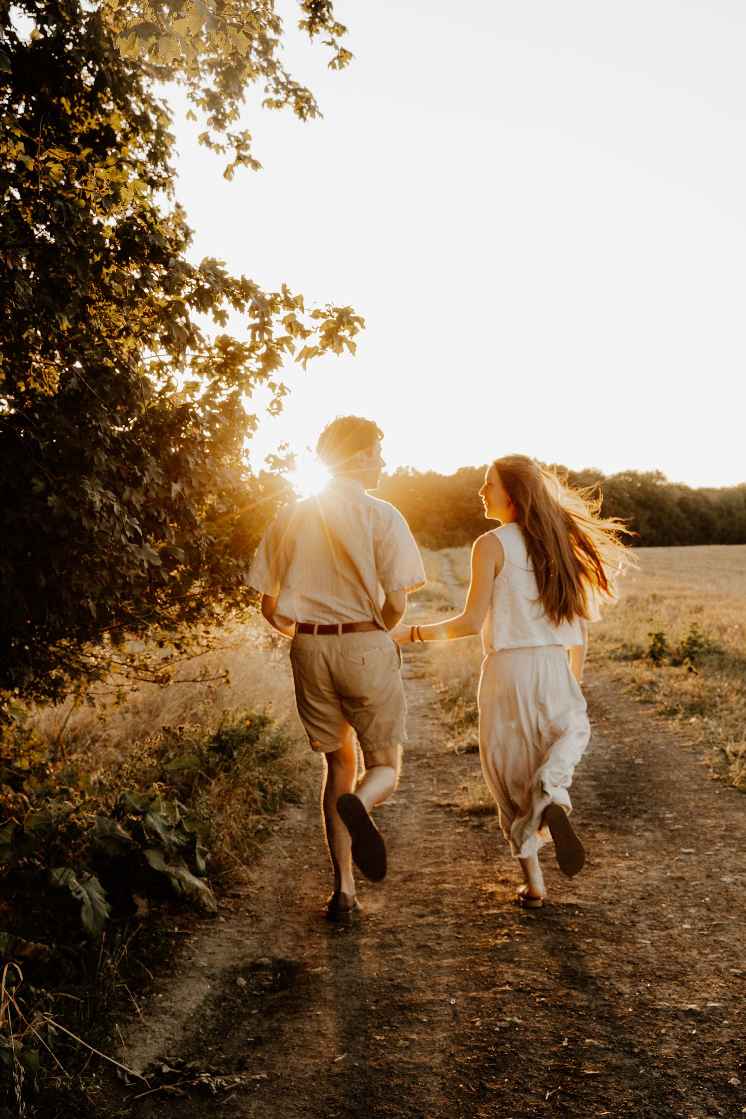 Séance photo de couple naturelle en extérieur, futurs mariés courant sur un chemin à la campagne.