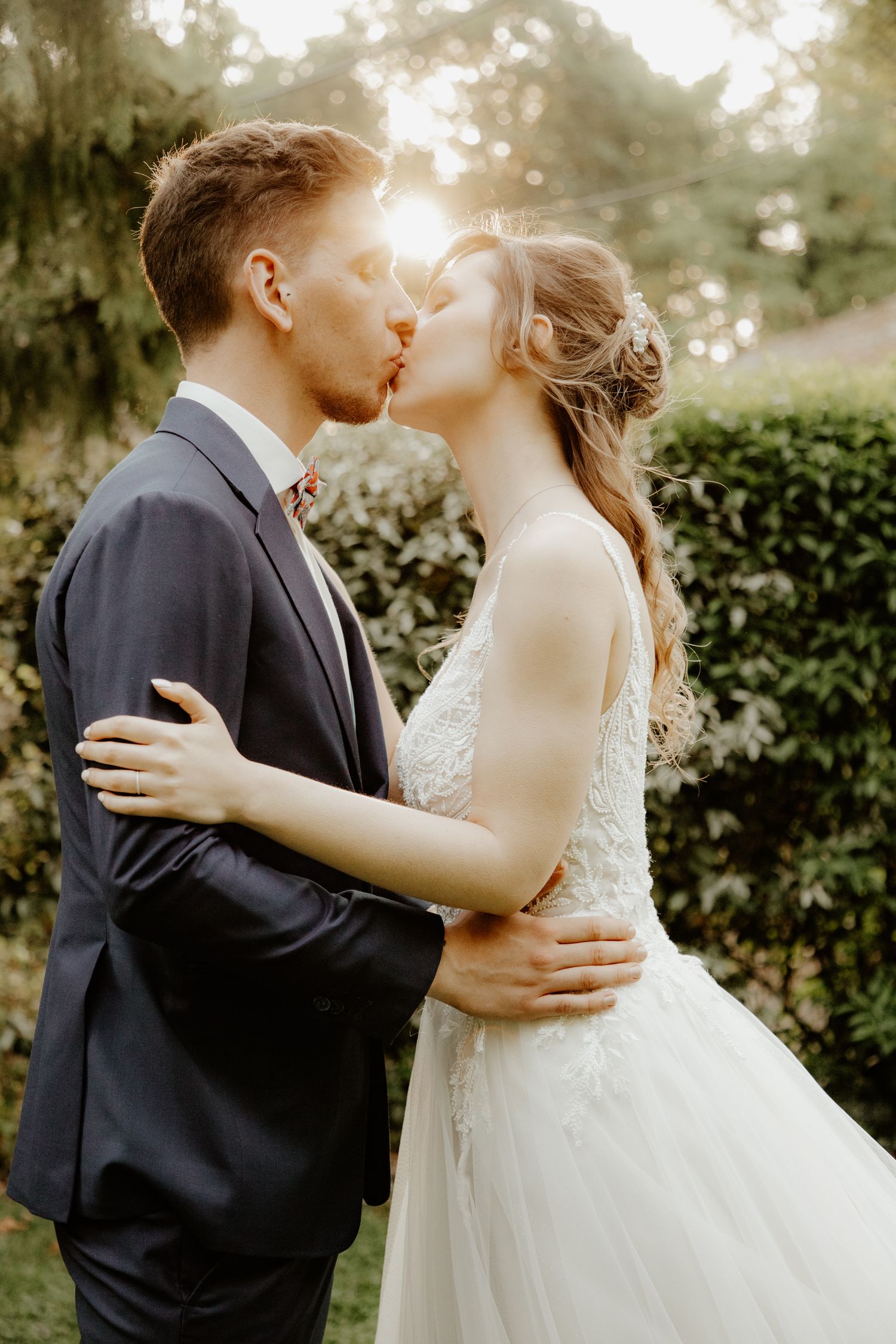 Séance photo de couple de mariés au coucher du soleil. Échange d'un baiser complice en pleine nature sous une lumière dorée.