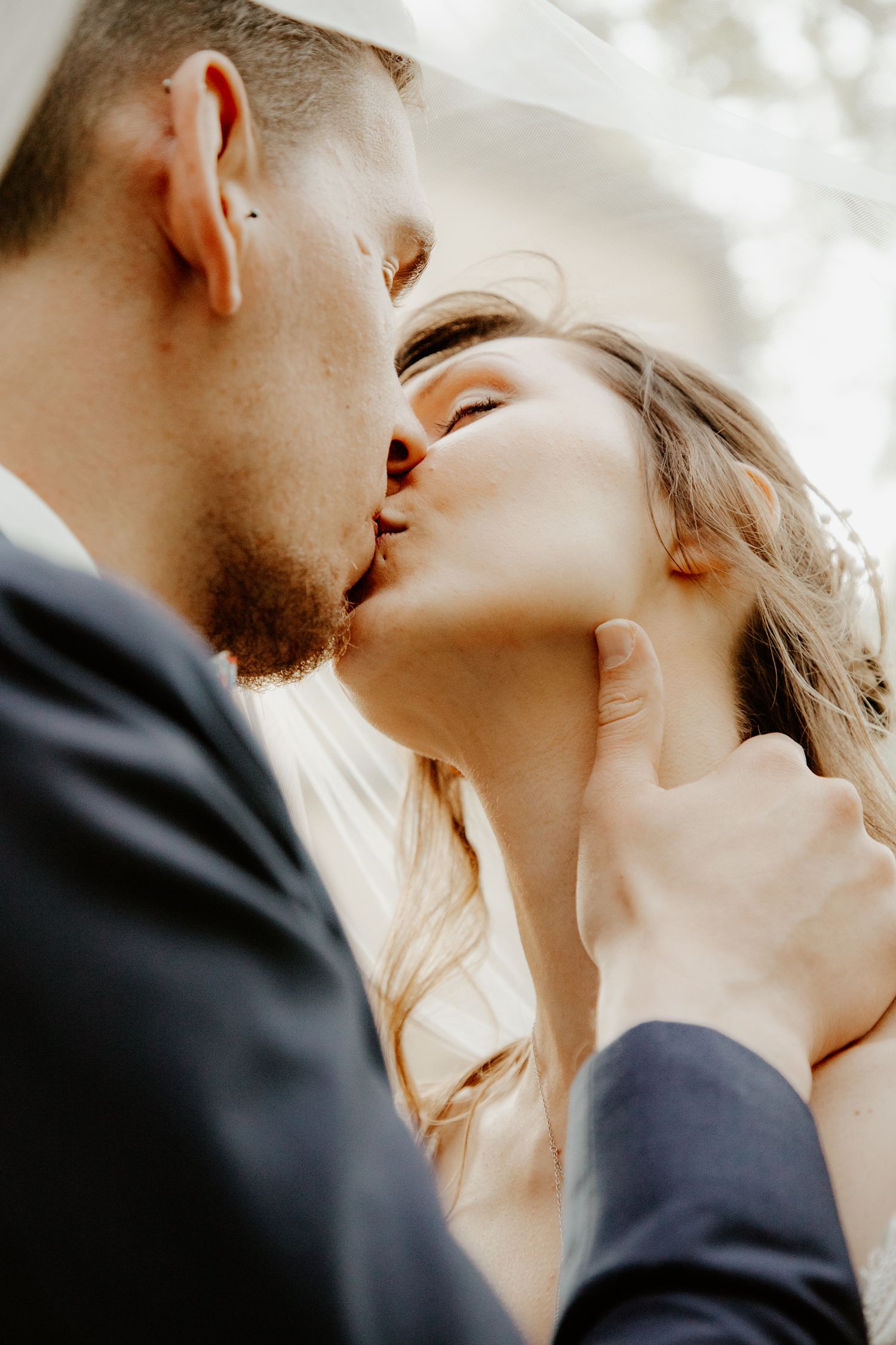 Baiser romantique d'un couple de mariés dissimulé sous le voile. Séance photo de couple par votre photographe.