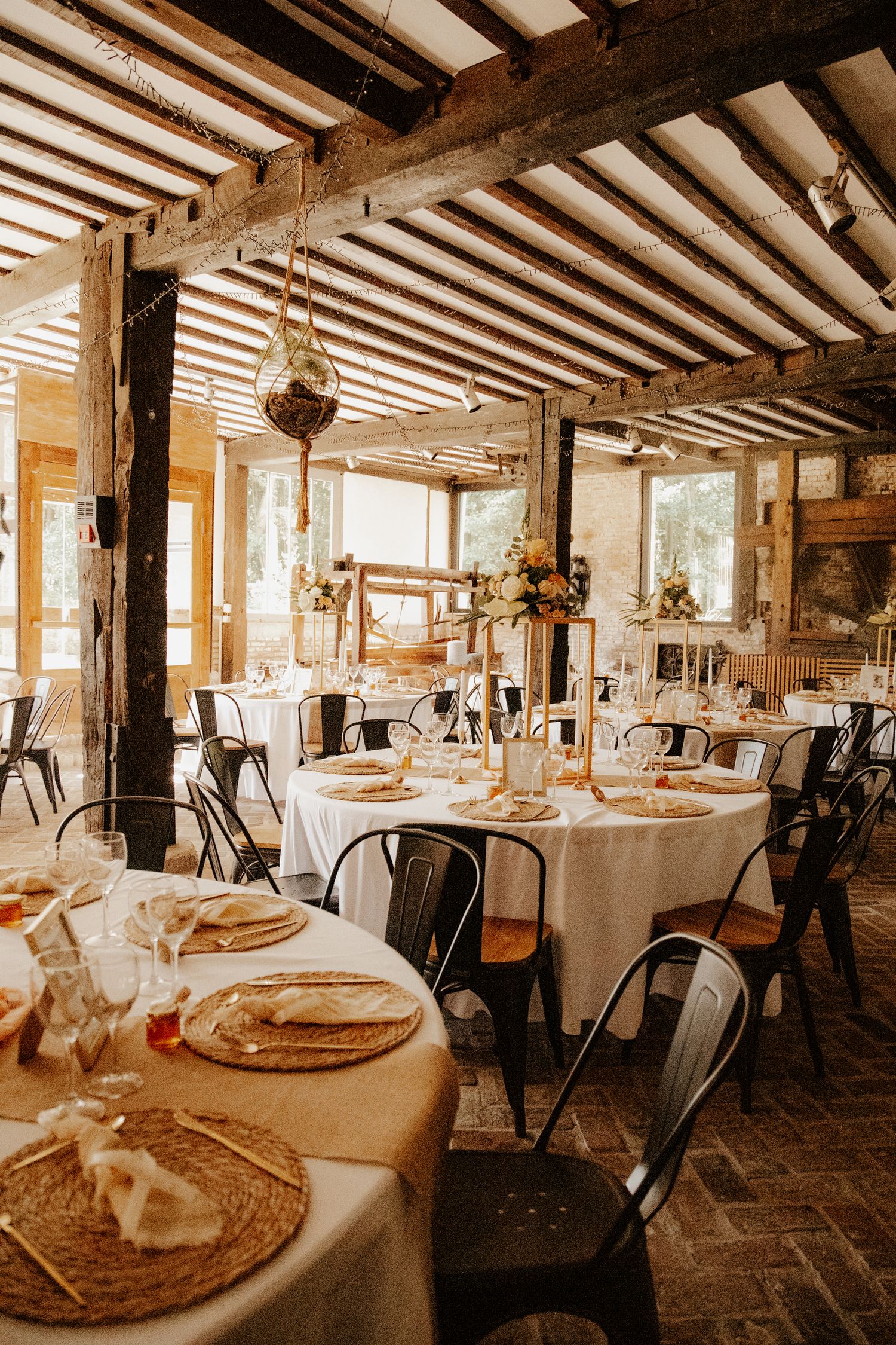 Décoration et tables dressées dans la salle de réception rustique avec poutres apparentes pour le dîner de mariage.