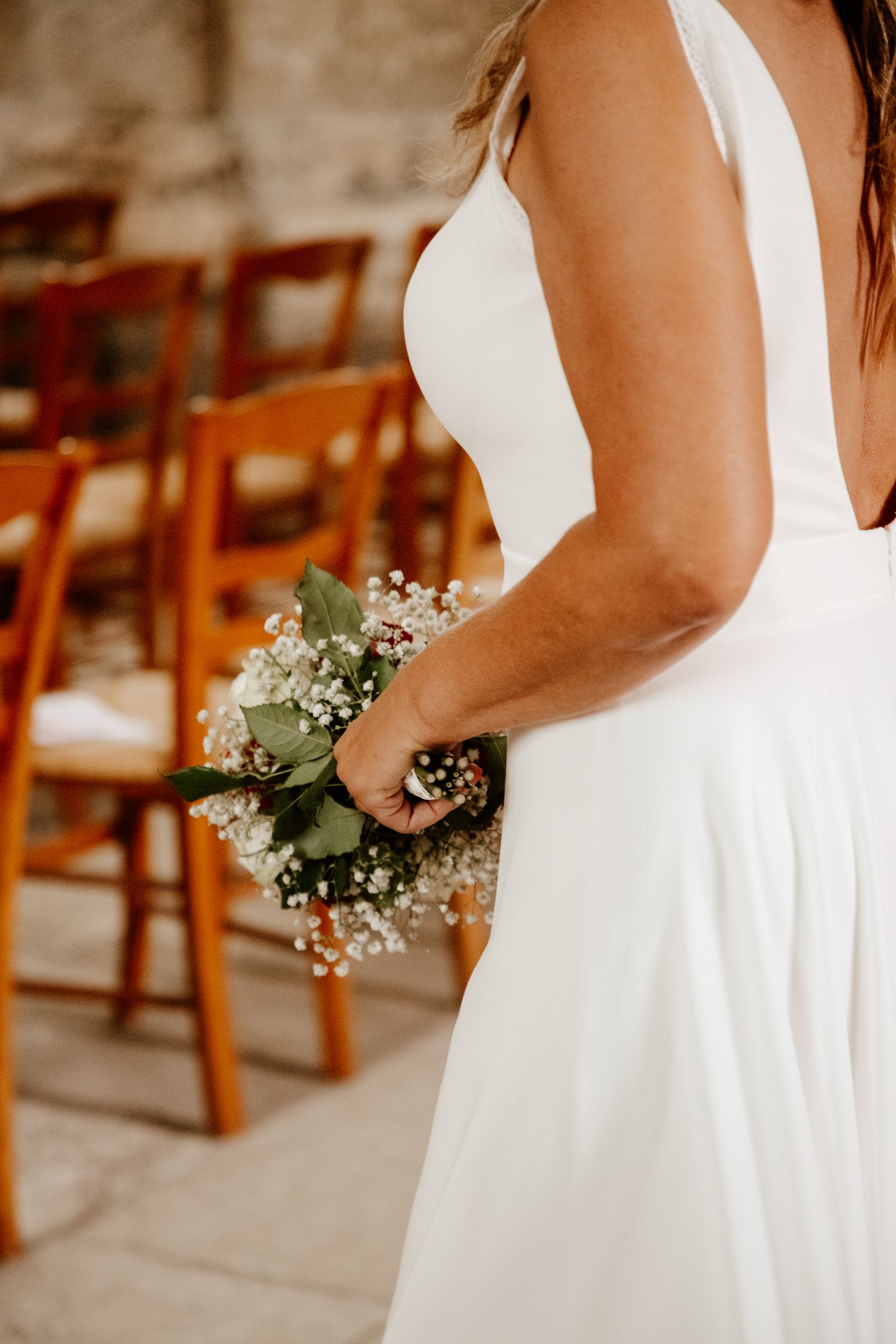 La mariée de dos avance dans l'allée de l'église, son bouquet de fleurs à la main, avant la cérémonie de mariage.