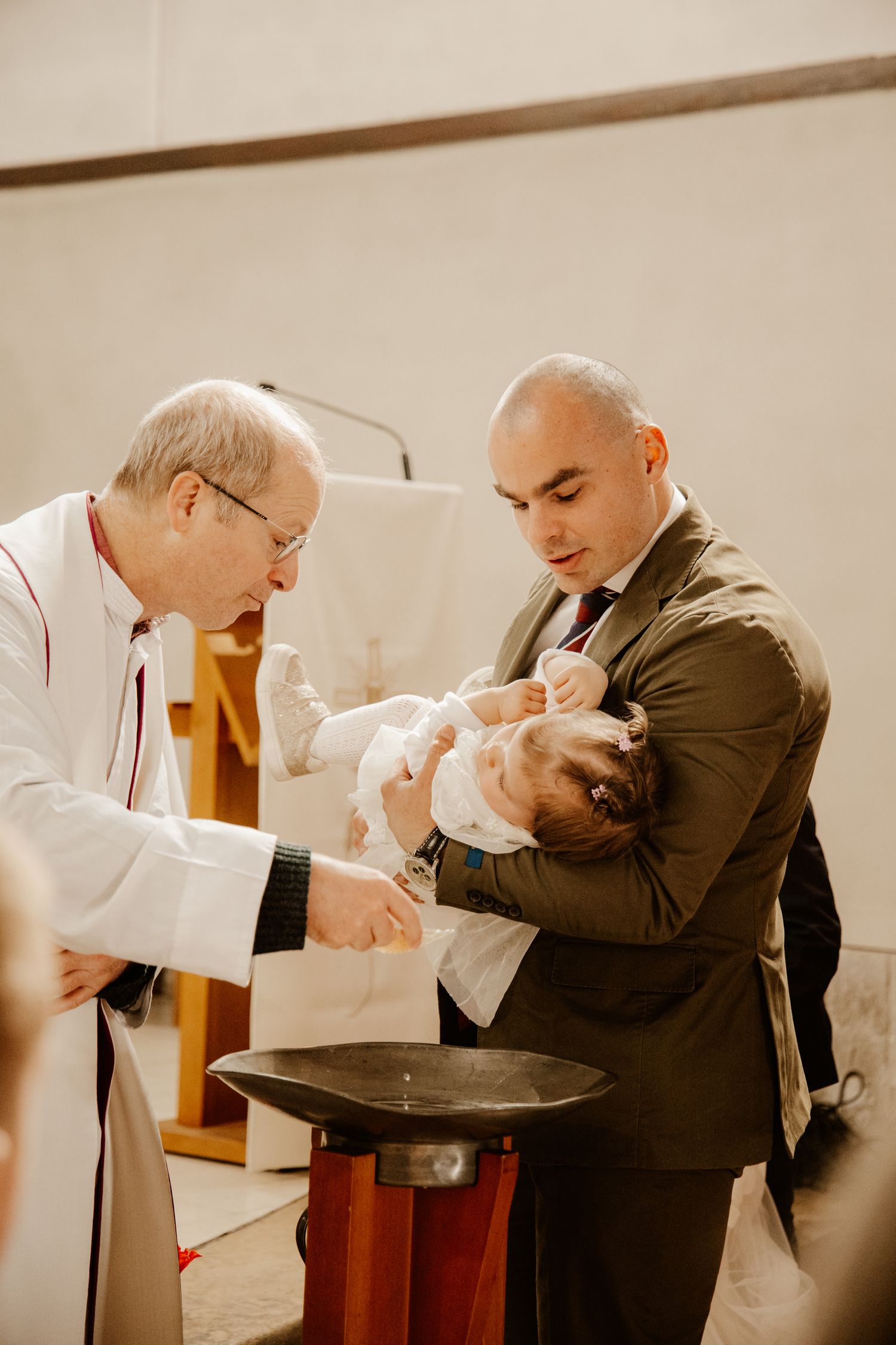 papa qui tien dans les bras sa fille qui se fait baptiser par le prêtre
